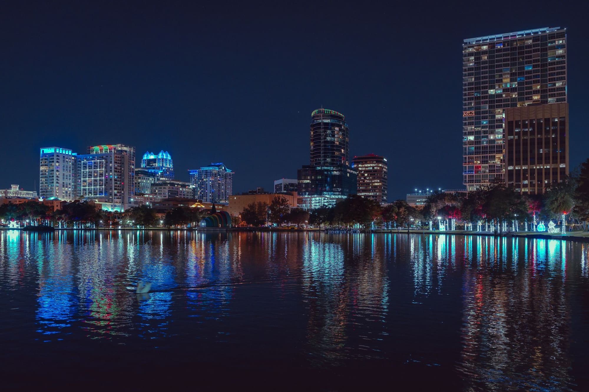 Stunning view of Orlando's city skyline illuminated over a tranquil lake at night.