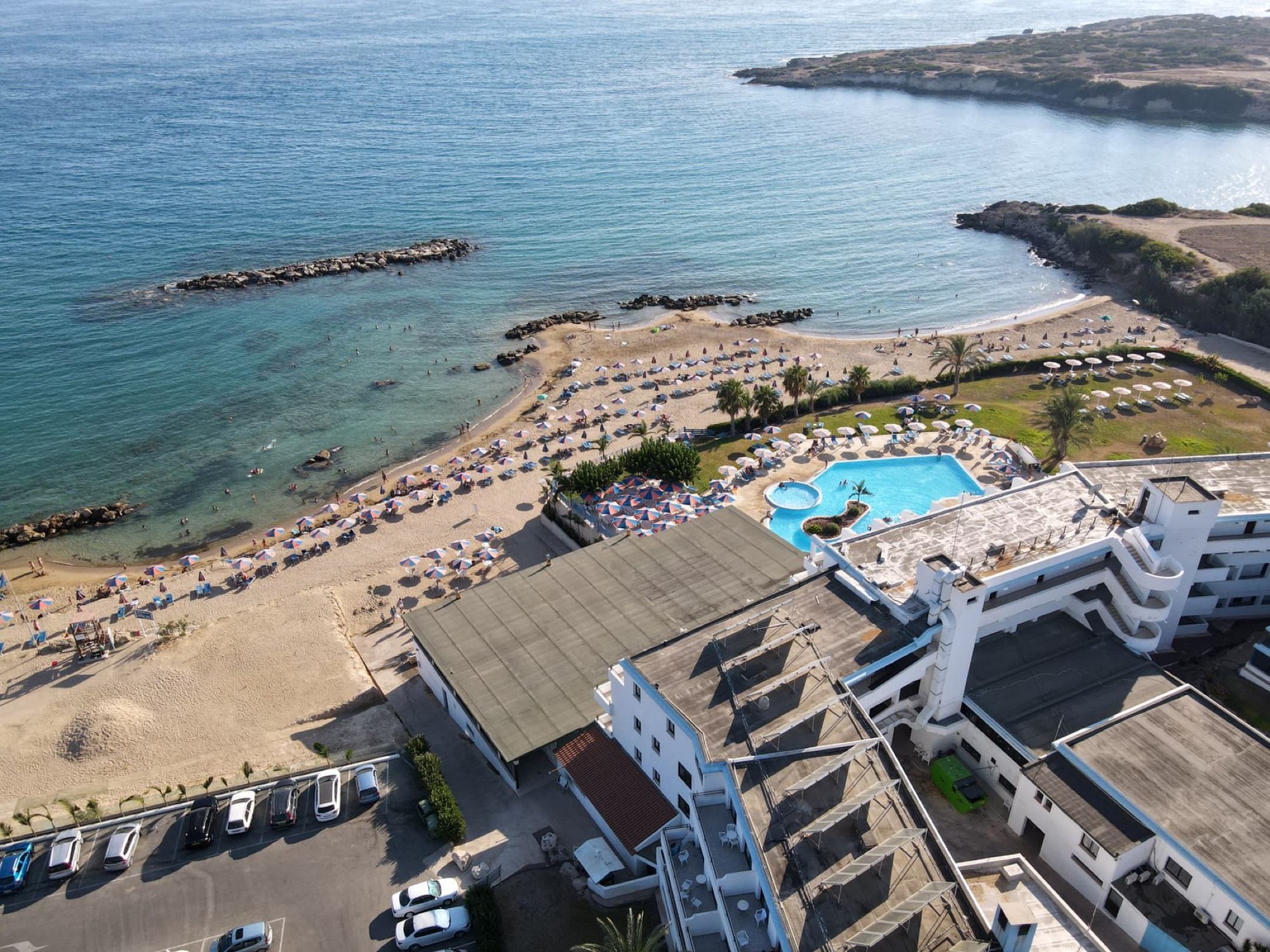 Aerial shot of a beachfront resort in Paphos, Cyprus showing beach, pool, and Mediterranean Sea.