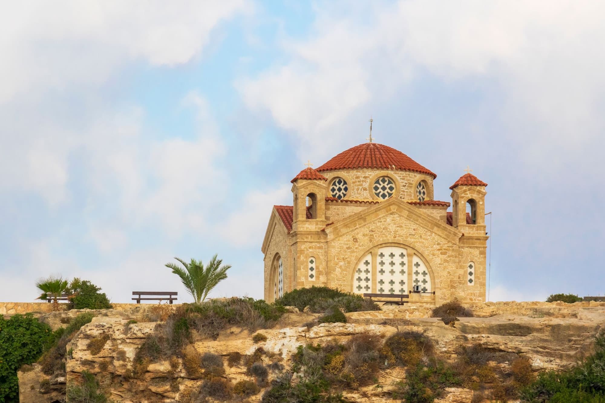 Scenic view of an Orthodox church on a cliff in Peyia, Paphos, Cyprus, under a cloudy sky.