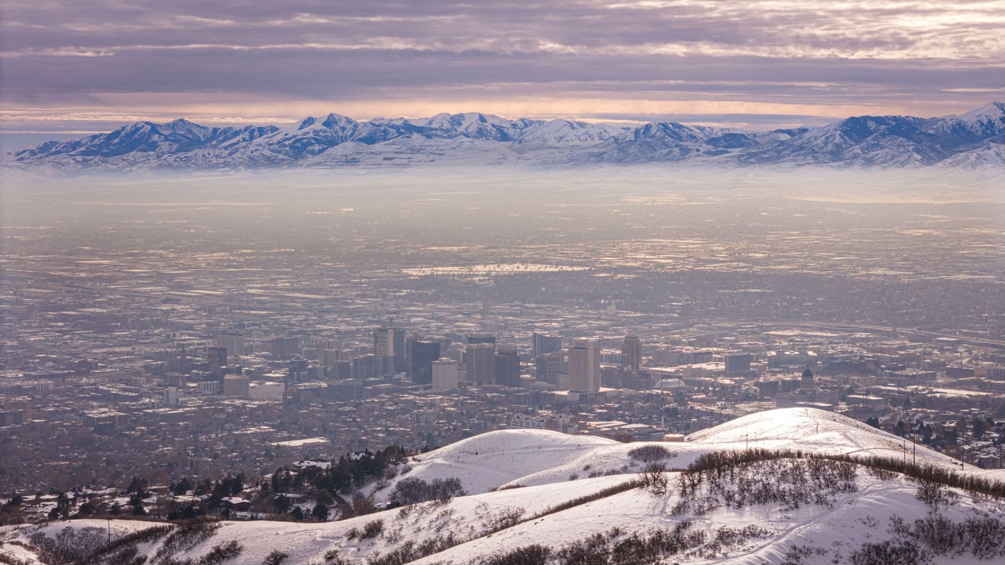 Aerial shot of snowy Salt Lake City with the Wasatch Mountains in the backdrop during winter.