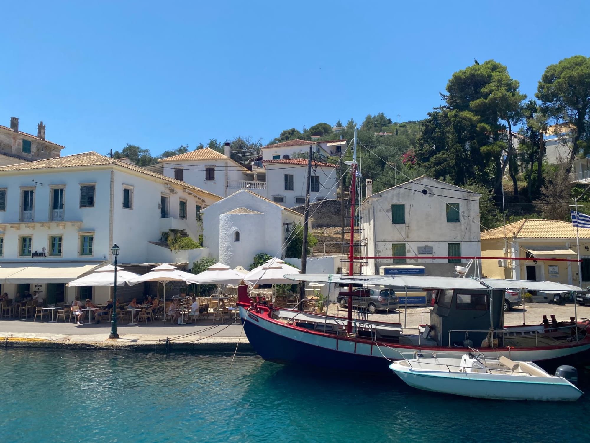 Idyllic scene of Gaios harbor in Paxos, Greece, with boats and traditional architecture under a bright summer sky.