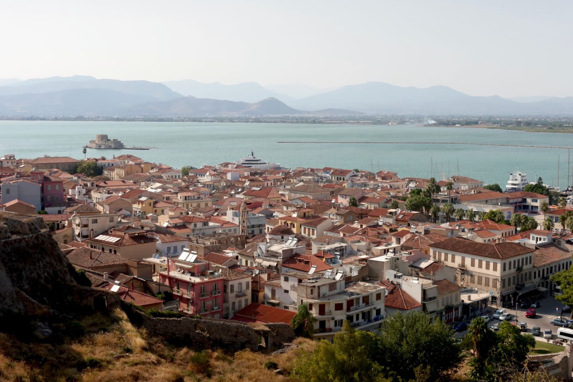 Aerial view of Nafplion, Greece, showcasing red rooftops and the serene sea with distant mountains.