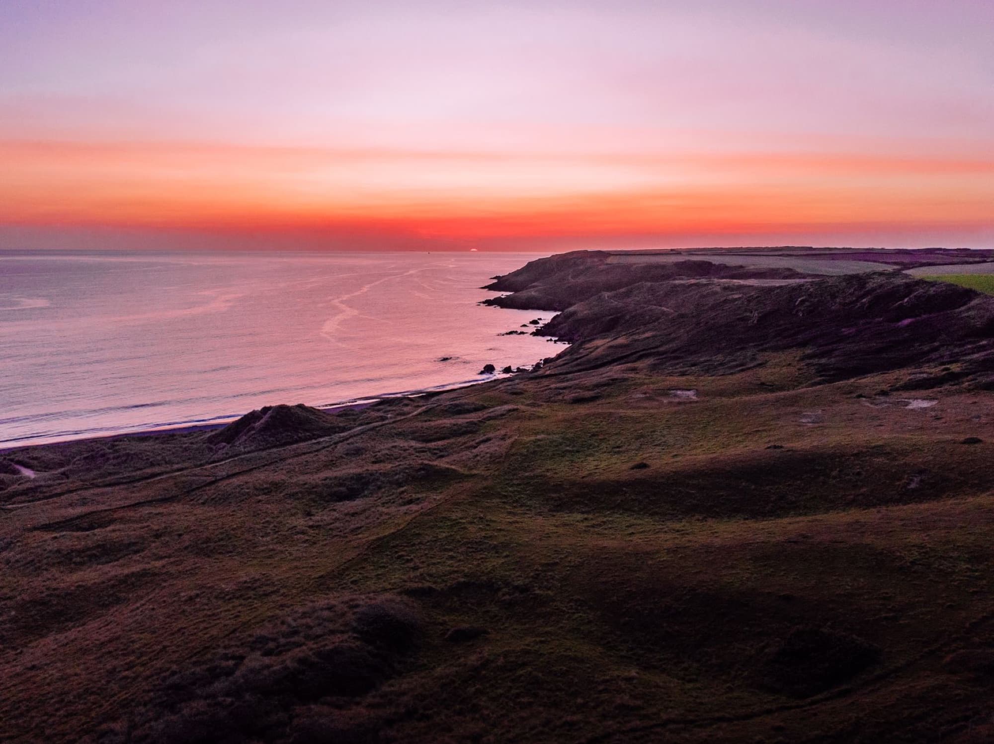 Dramatic sunset over Pembrokeshire coast in Wales, highlighting sea and rocky shoreline.
