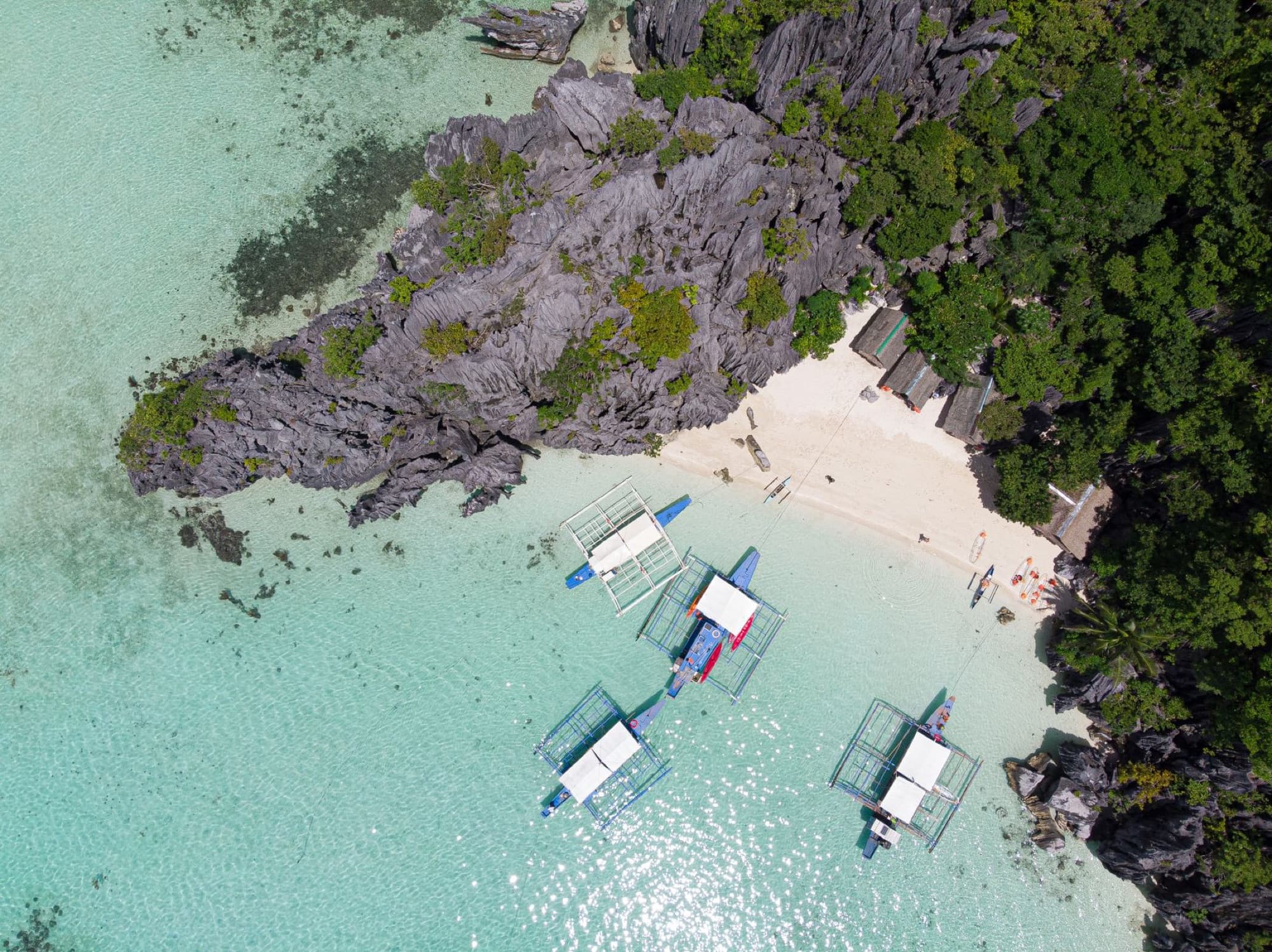 Aerial view of boats on clear turquoise water along the sandy beach and lush forest in the Philippines.