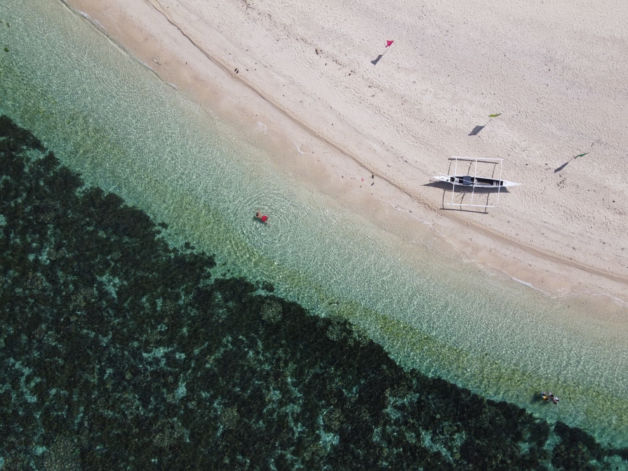 Aerial shot of a banca near a sandy beach in Romblon, Philippines. Clear blue waters and beach scenery.