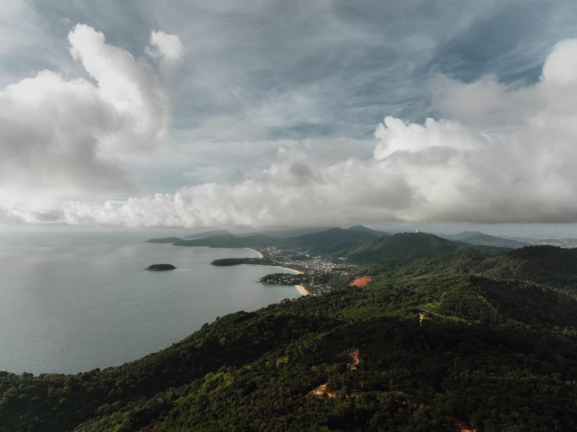 Stunning aerial view of Phuket's lush hills and coastline under a cloudy sky.