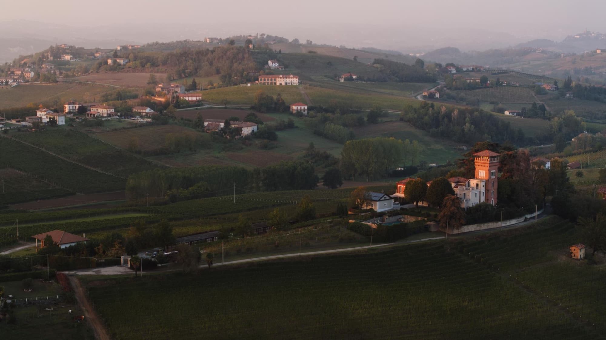 A breathtaking drone shot of Piedmont's lush vineyards and rolling hills at sunset, highlighting the serene rural landscape.