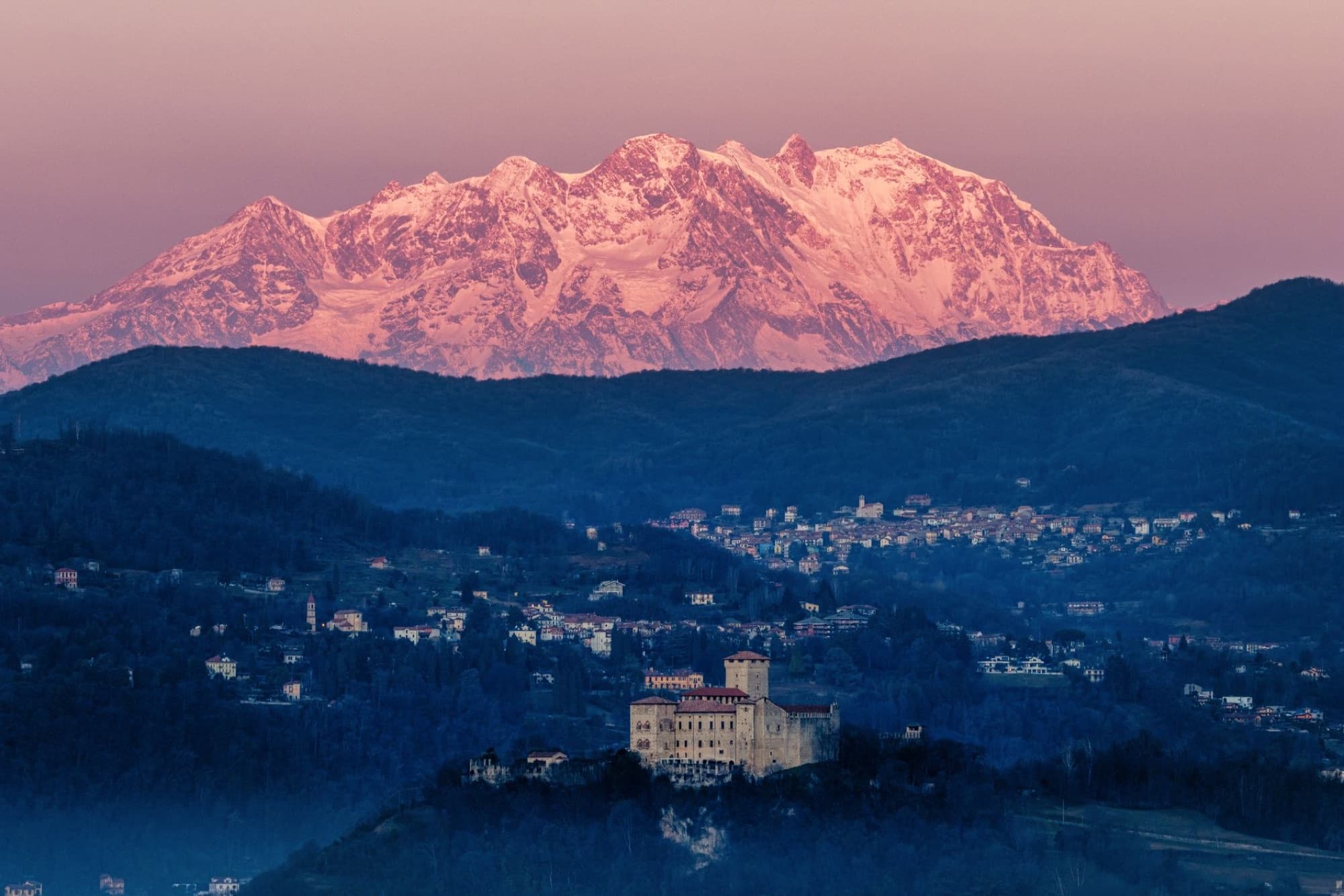 Beautiful view of Italian village with Alps in the background at sunset, creating a dramatic landscape.