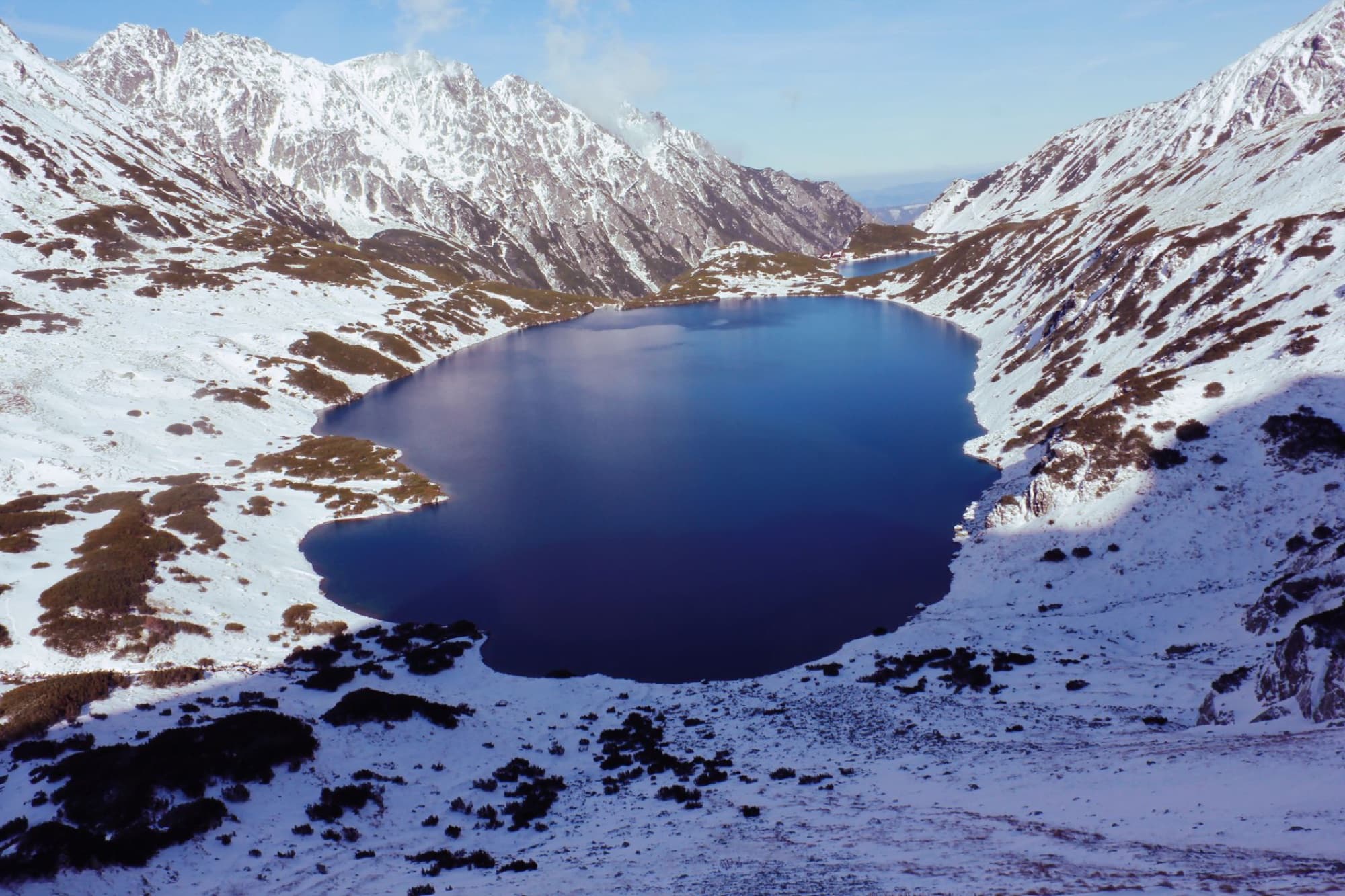 Breathtaking winter view of snow-covered mountains surrounding a serene mountain lake in Poland.