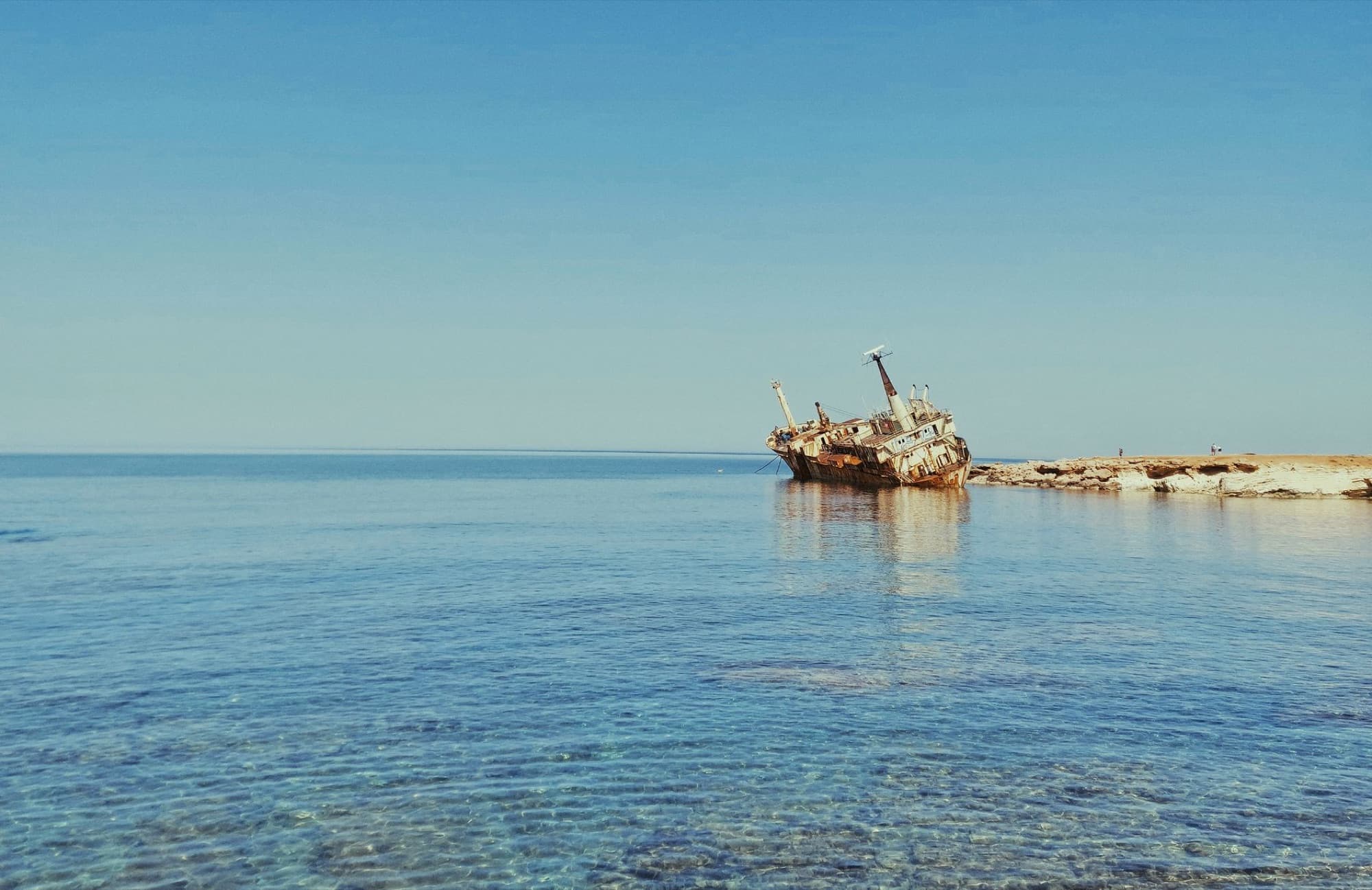A scenic view of an abandoned shipwreck near the coast of Paphos, Cyprus, under a clear blue sky.