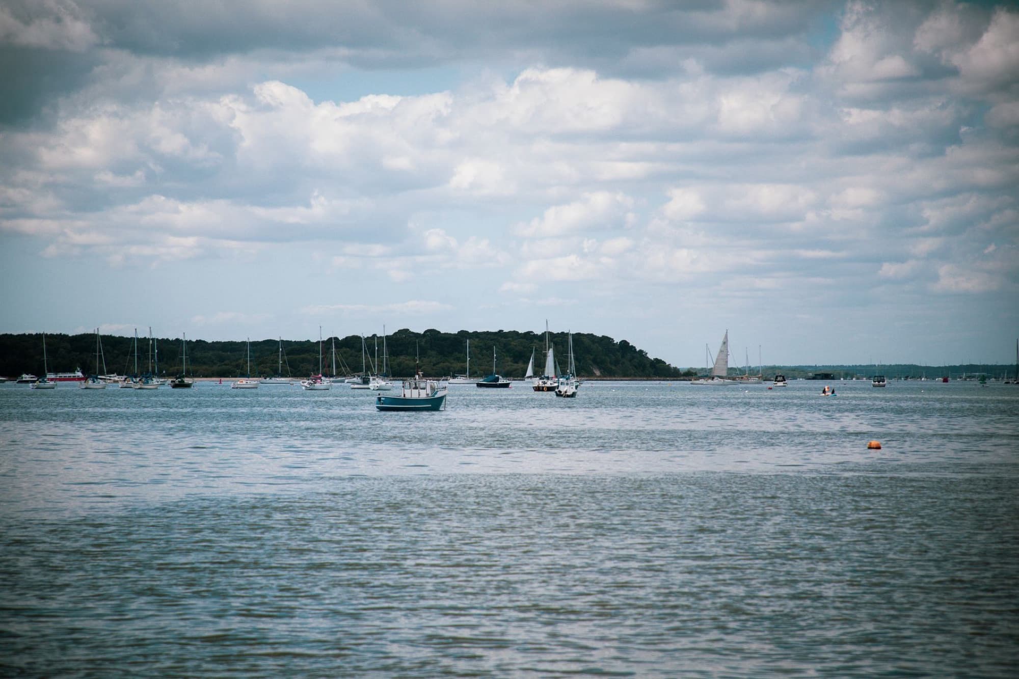 Tranquil view of sailboats anchored at Poole Harbor under a cloudy sky.