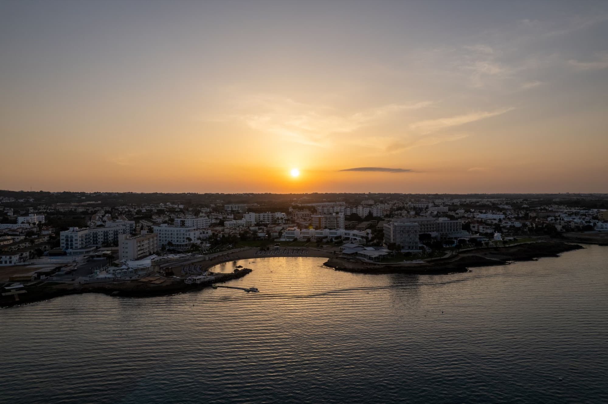 Aerial view of a sunset over Pernera Bay, showcasing buildings and the coastline in Famagusta, Cyprus.