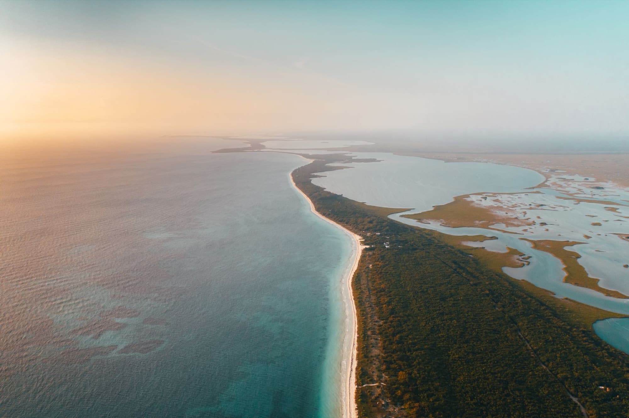 Stunning aerial shot of a tranquil Mexican beach merging with lush landscapes under a serene sunset sky.