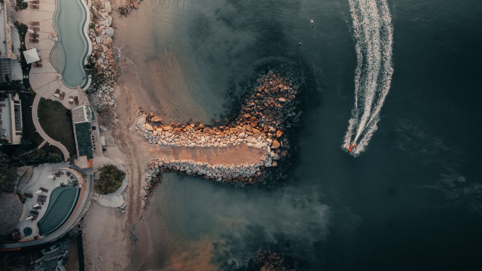 Aerial drone view of a resort by the ocean with a rocky coastline and boat in Puerto Vallarta, Mexico.