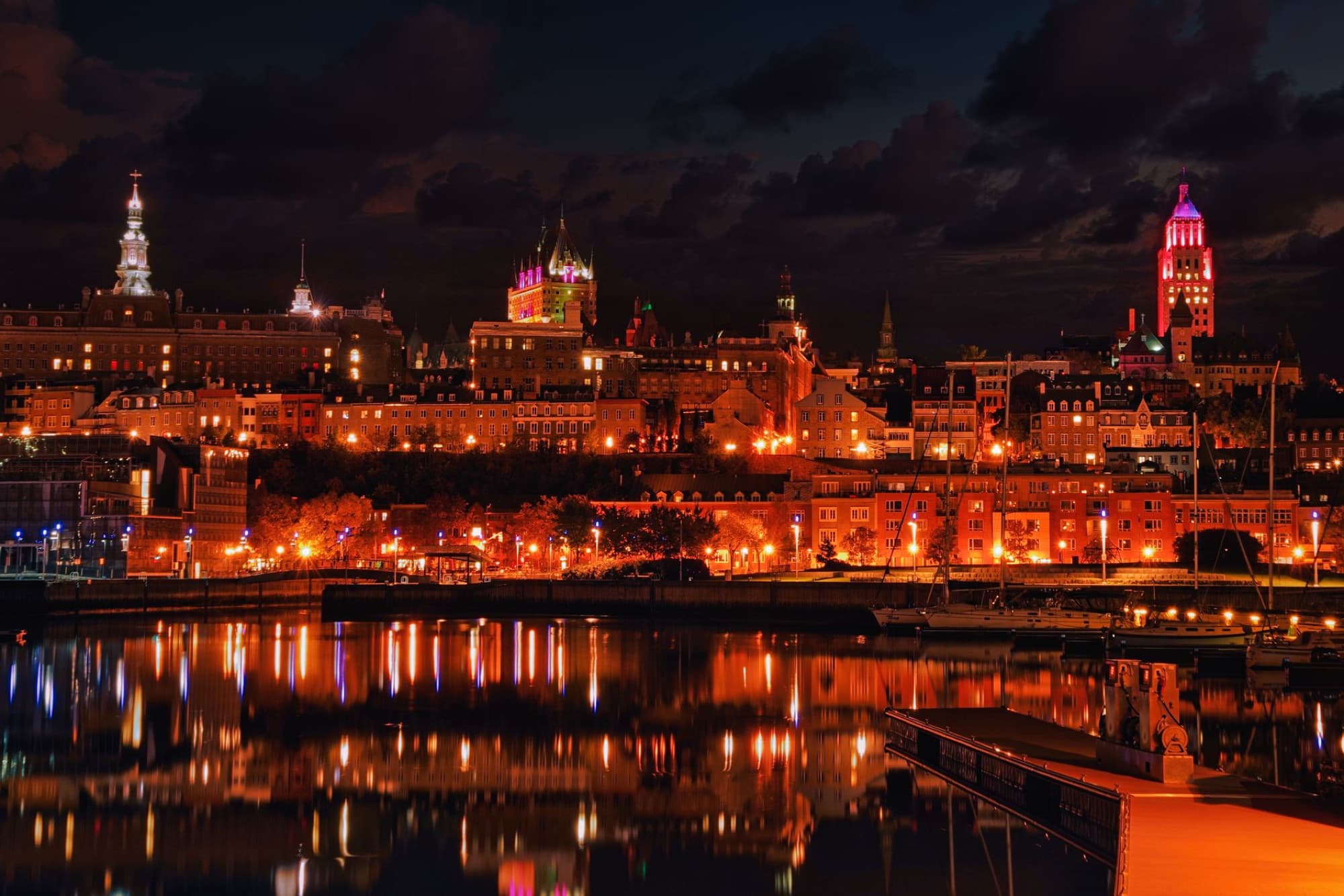 Stunning night view of Quebec City skyline reflecting on water, showcasing vibrant city lights.
