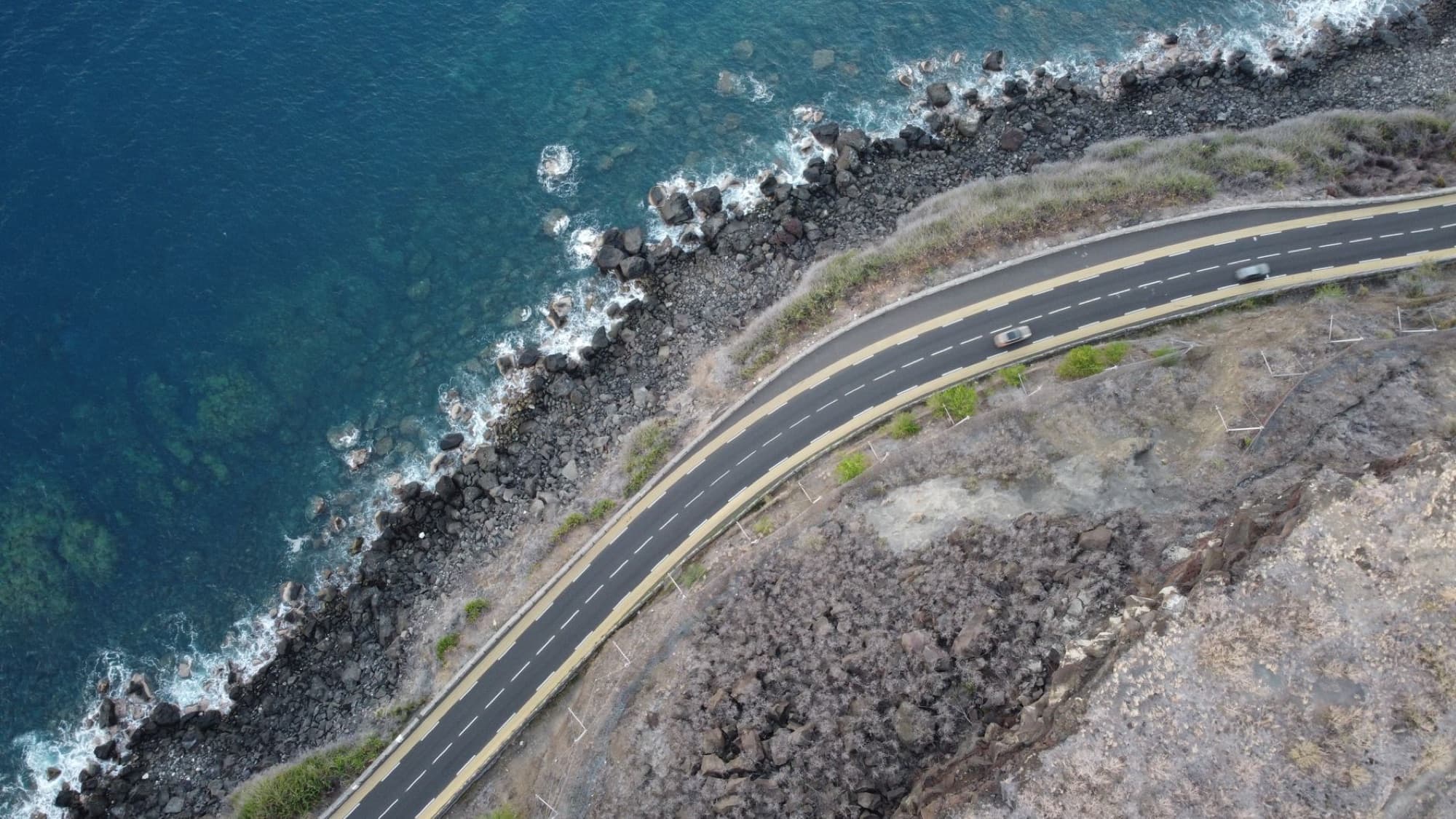 A stunning aerial view of a winding coastal road in La Réunion, France, beside the rocky shoreline.