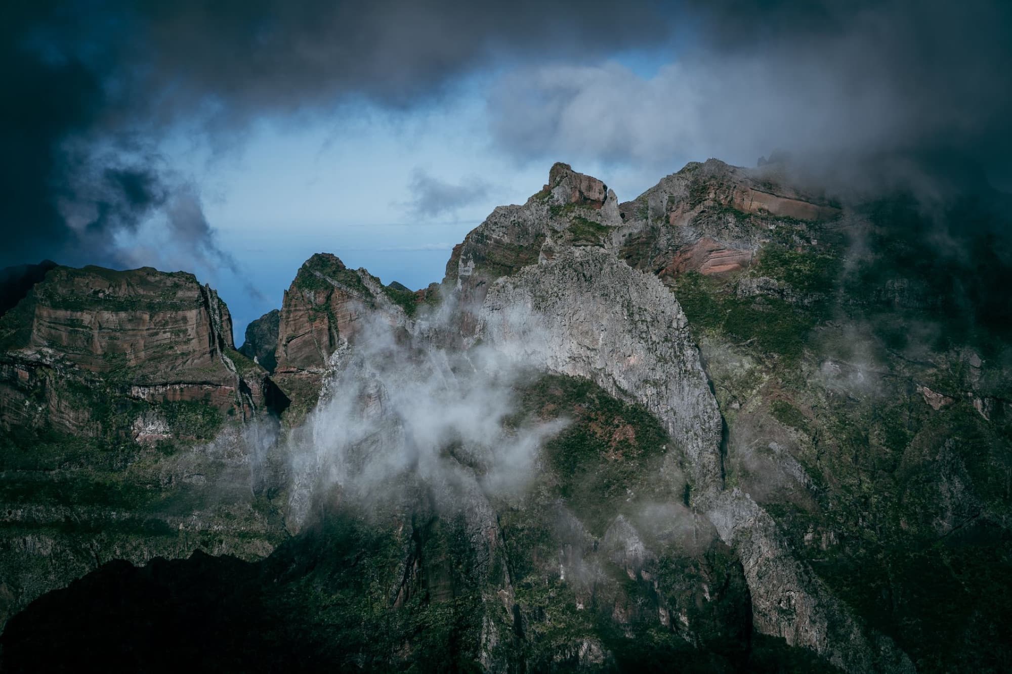 A stunning aerial photograph capturing eroded mountain peaks shrouded in clouds and mist, creating a dramatic nature scene.
