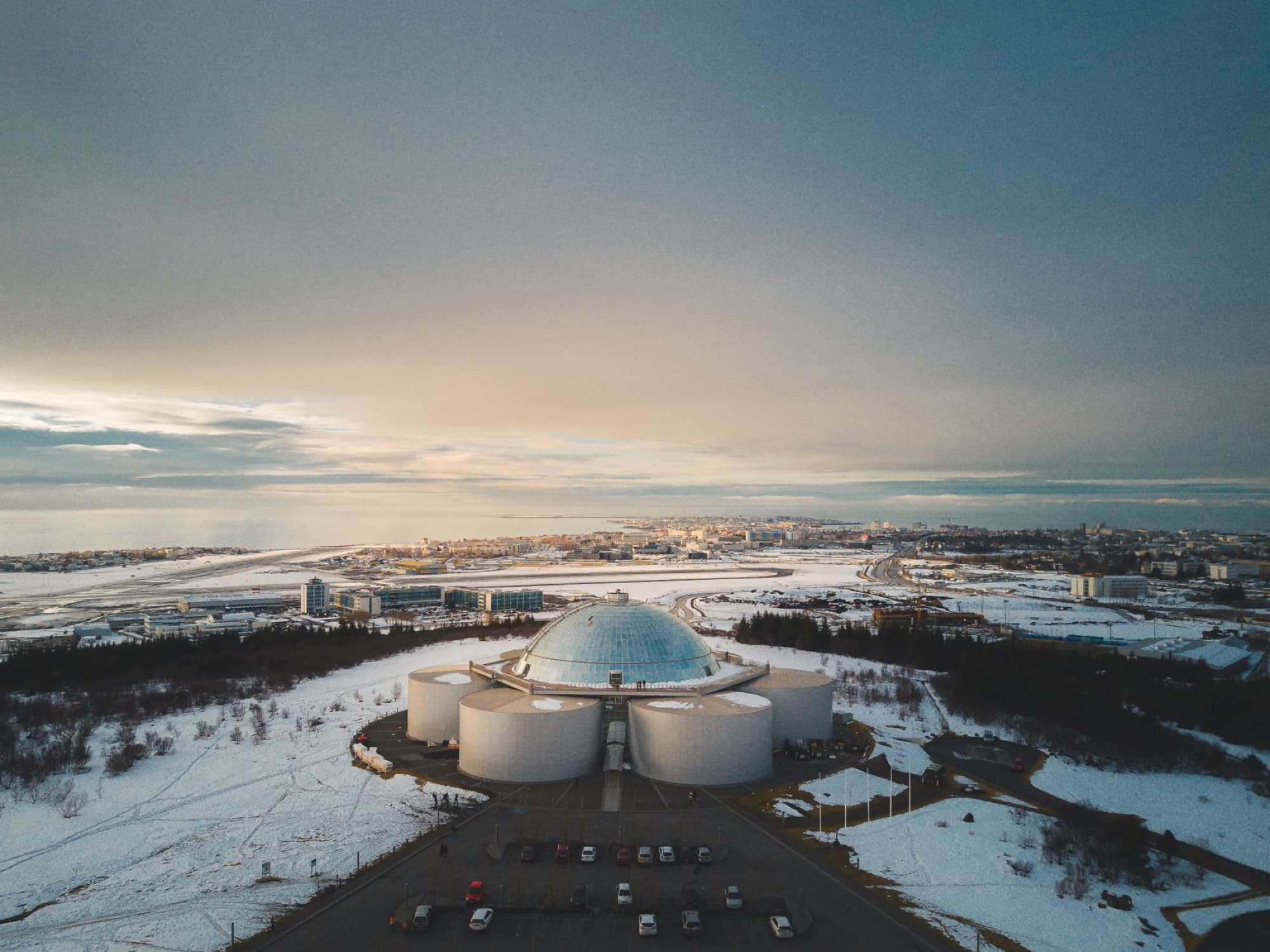 Aerial shot showcasing Perlan landmark against the backdrop of Reykjavik's snowy urban landscape.