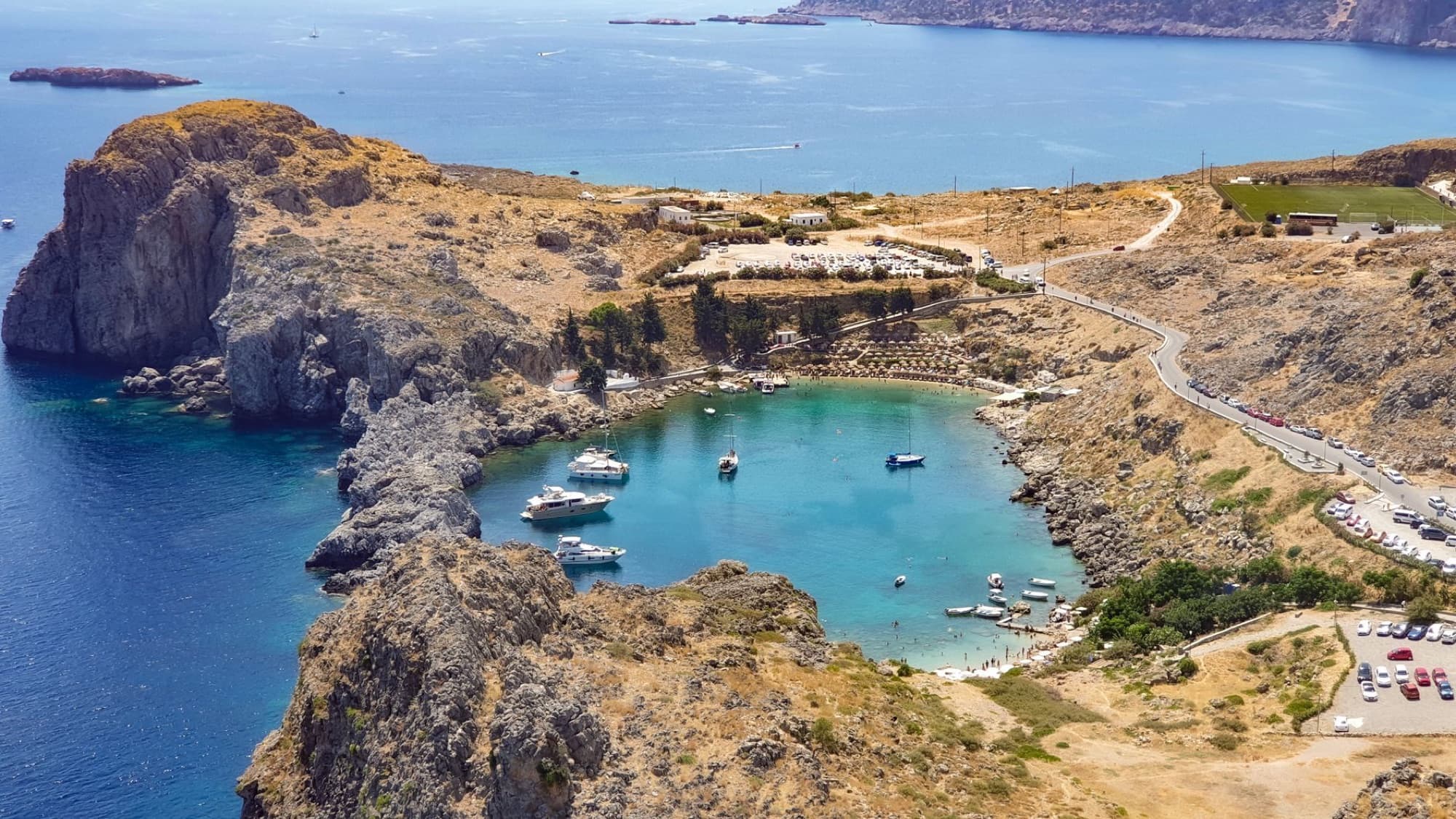 Stunning aerial view of Saint Paul's Bay in Rhodes, Greece. Turquoise waters, boats, and rocky cliffs.