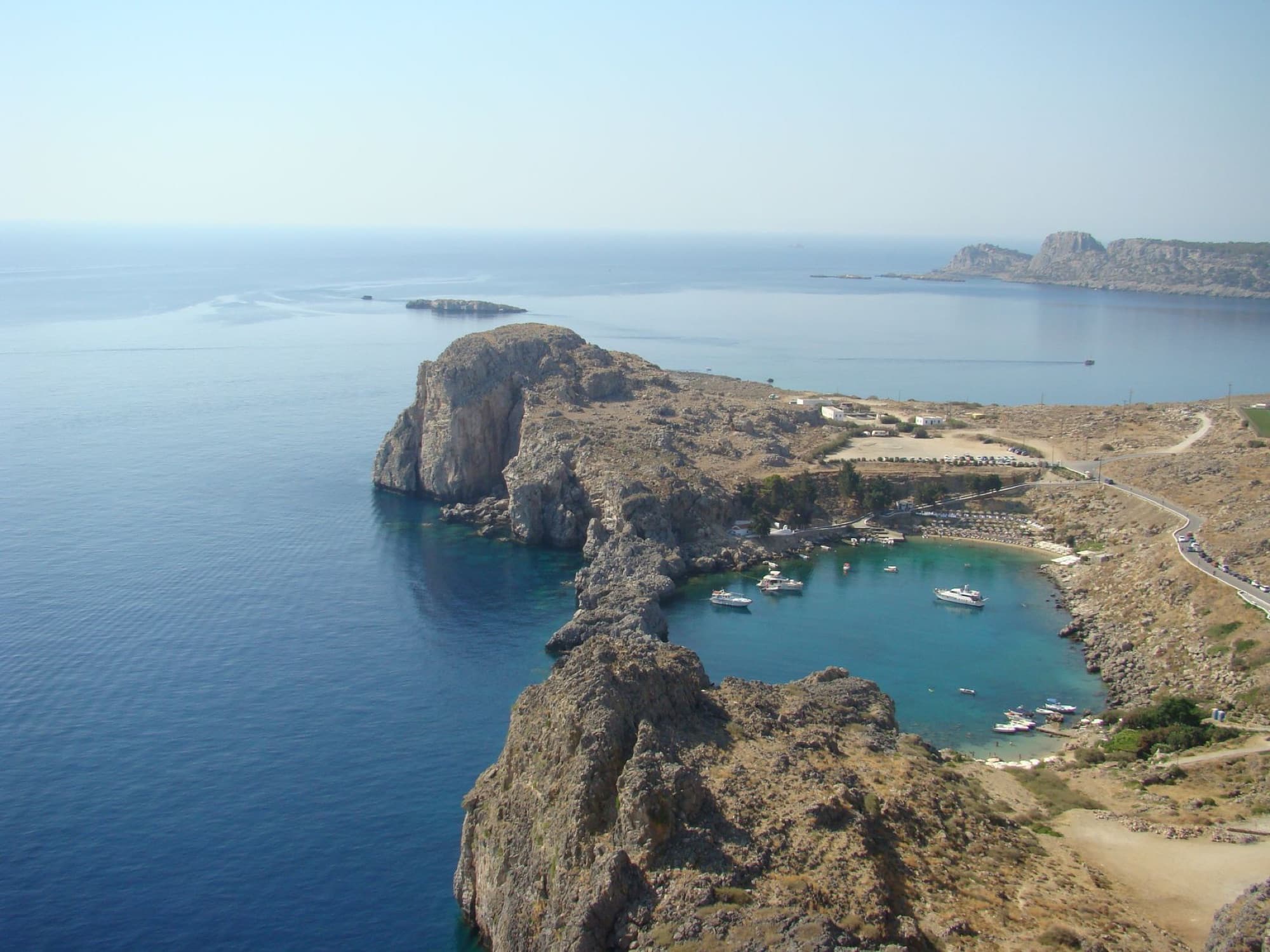 A stunning aerial shot of Lindos Bay in Rhodes, Greece, showcasing clear blue waters and rugged cliffs.