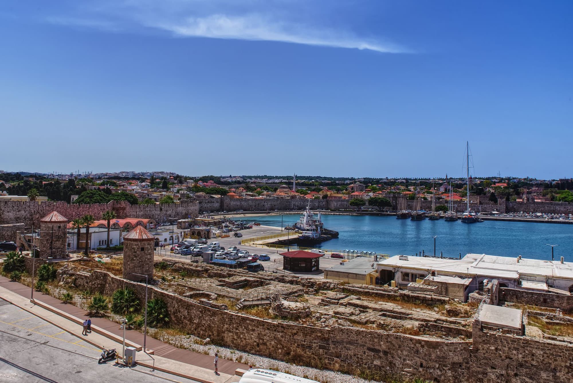 Aerial view of Rhodes Town's historic port and ancient walls under a clear blue sky.