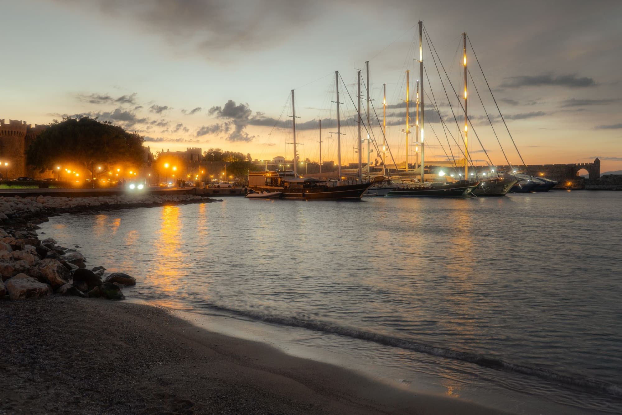 Beautiful sunset at Rhodes Harbor, Greece with yachts and city lights reflecting on the water.