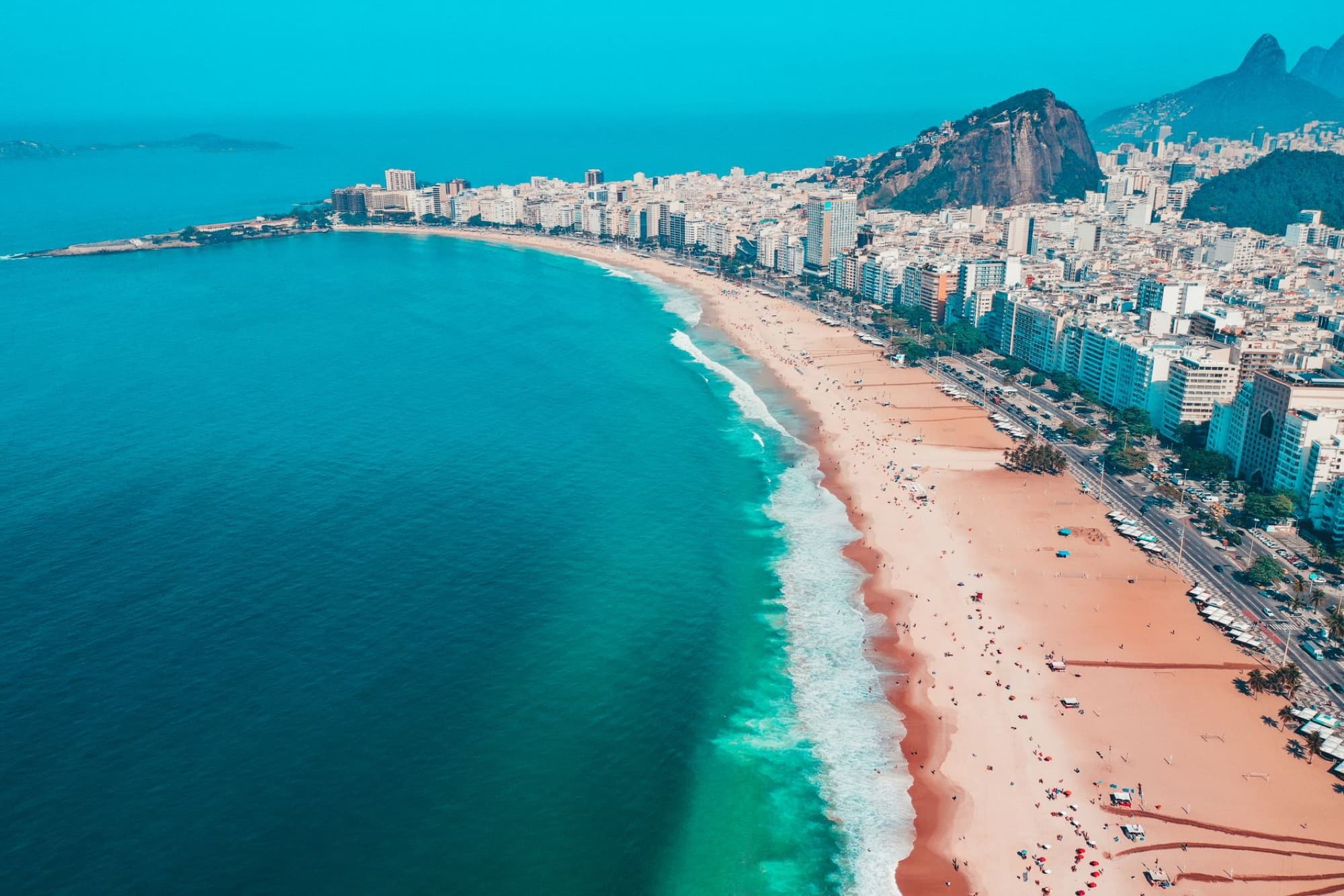 Vibrant aerial view of Copacabana Beach, Rio de Janeiro, with city skyline and mountains.
