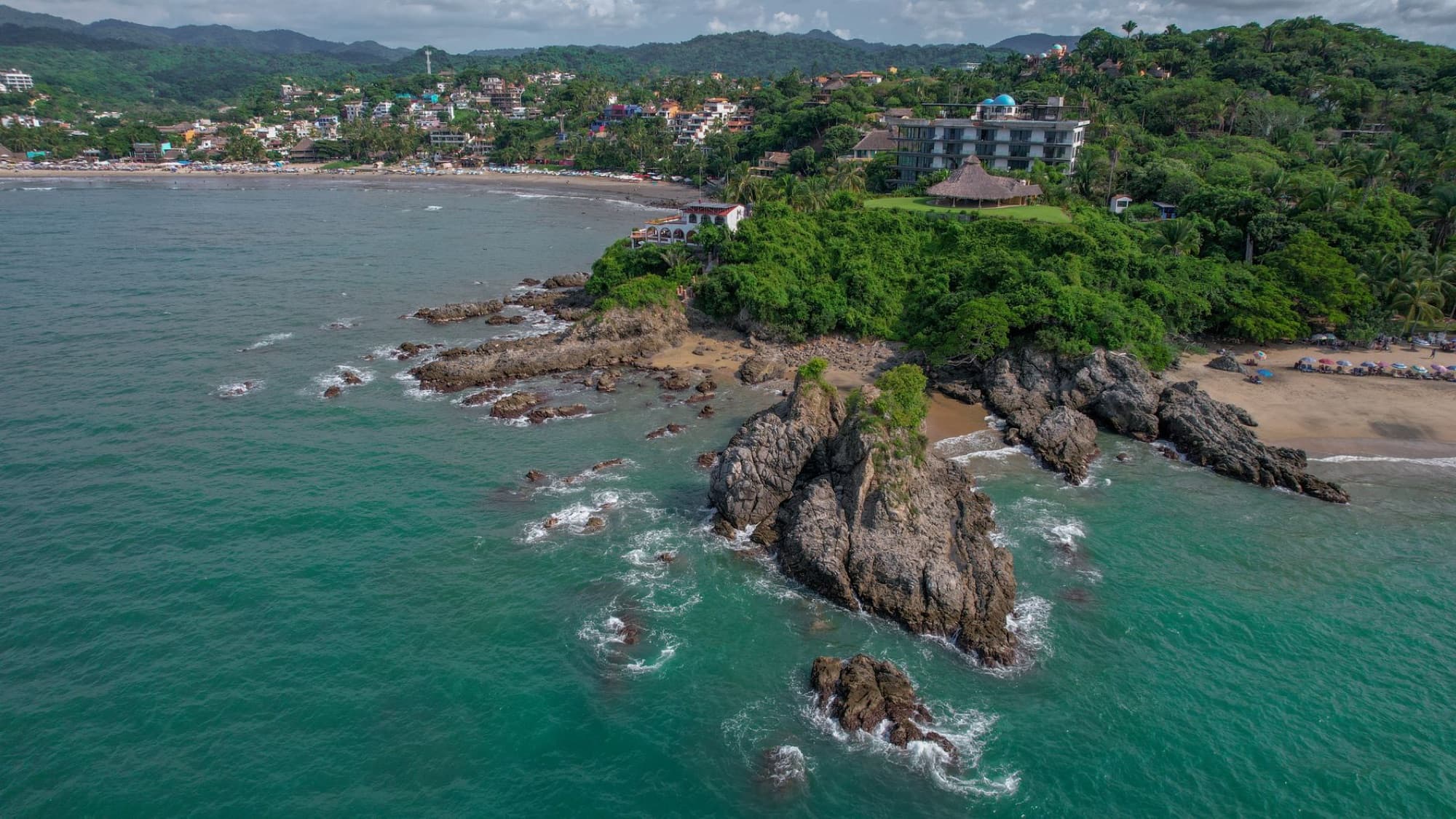 Scenic aerial view of rocky coastline and lush greenery on a tropical beach.