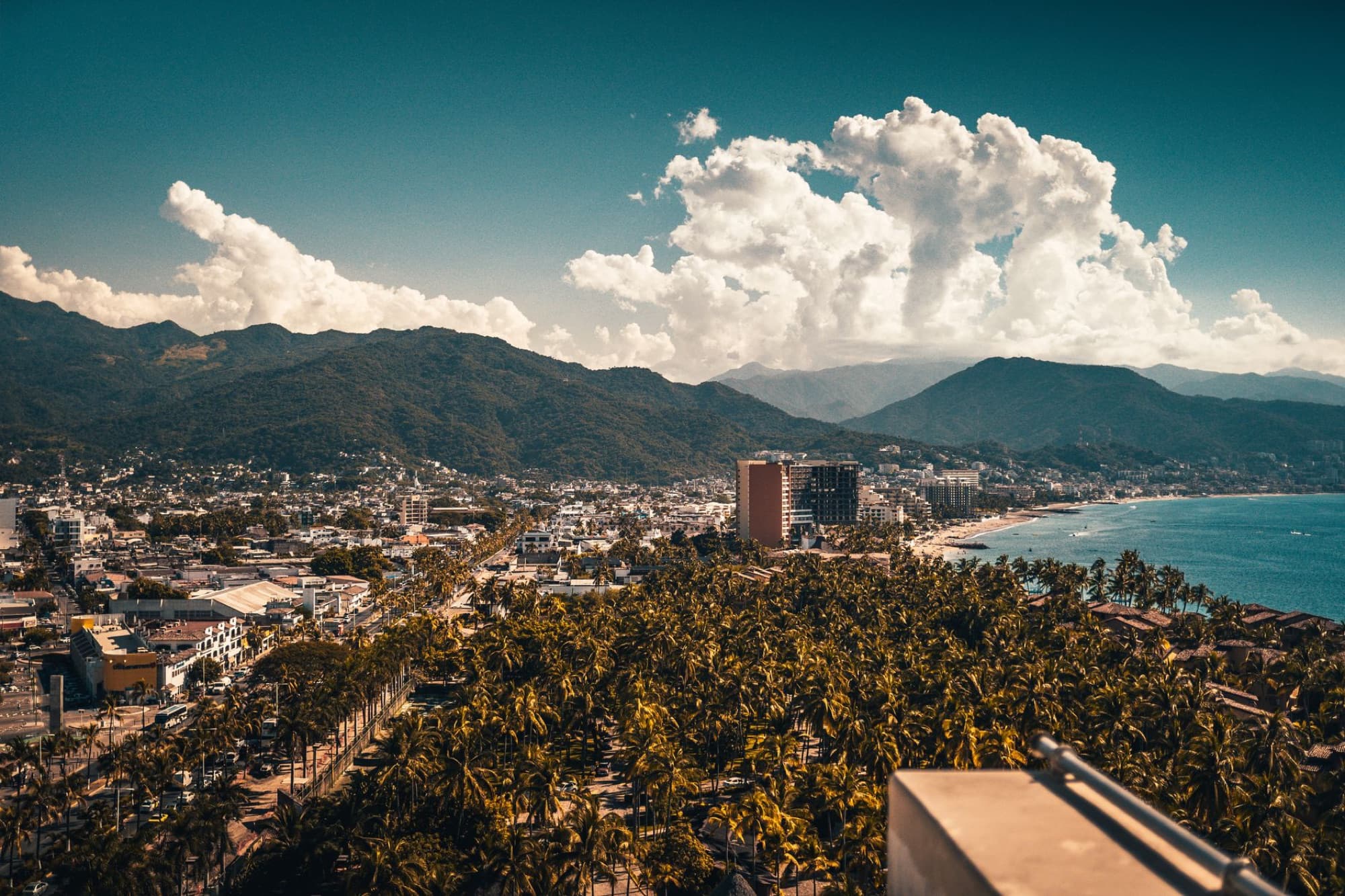 A breathtaking aerial view of Puerto Vallarta, showing mountains, cityscape, palm trees, and coastline under a clear sky.