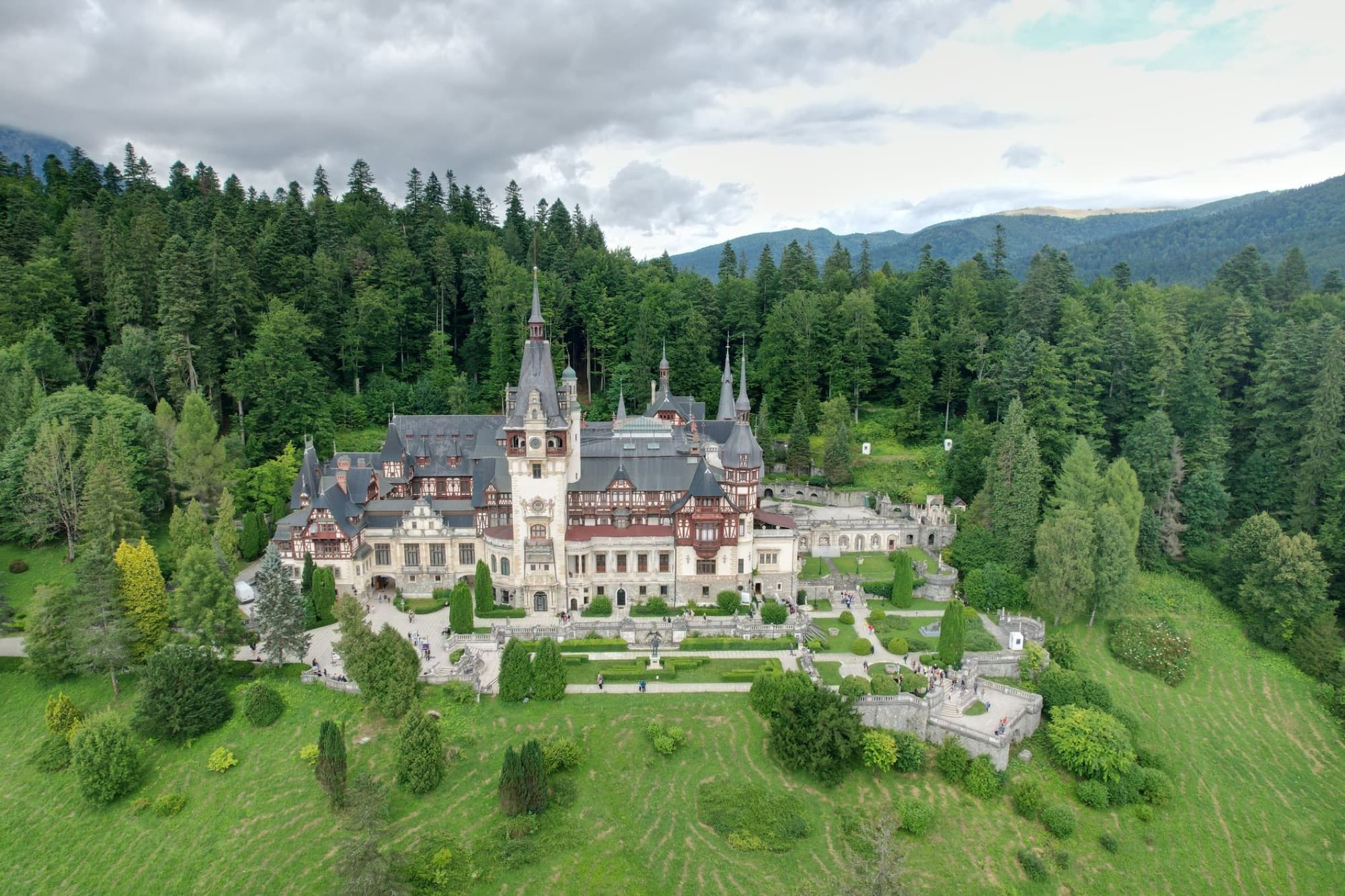Stunning drone shot of Peles Castle surrounded by lush forest in Romania.