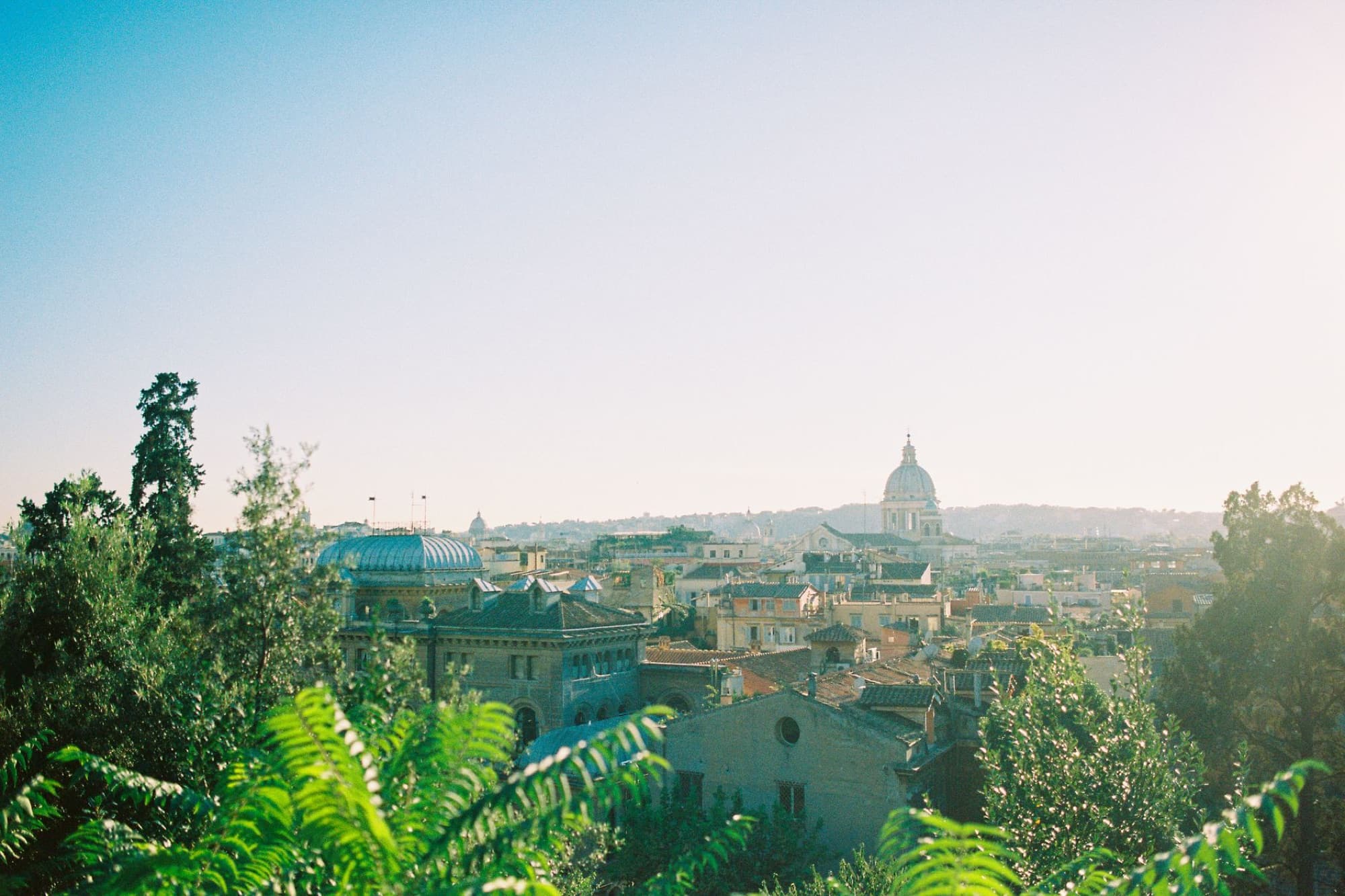 Beautiful aerial view of Rome's skyline with lush greenery and historic architecture under a clear blue sky.