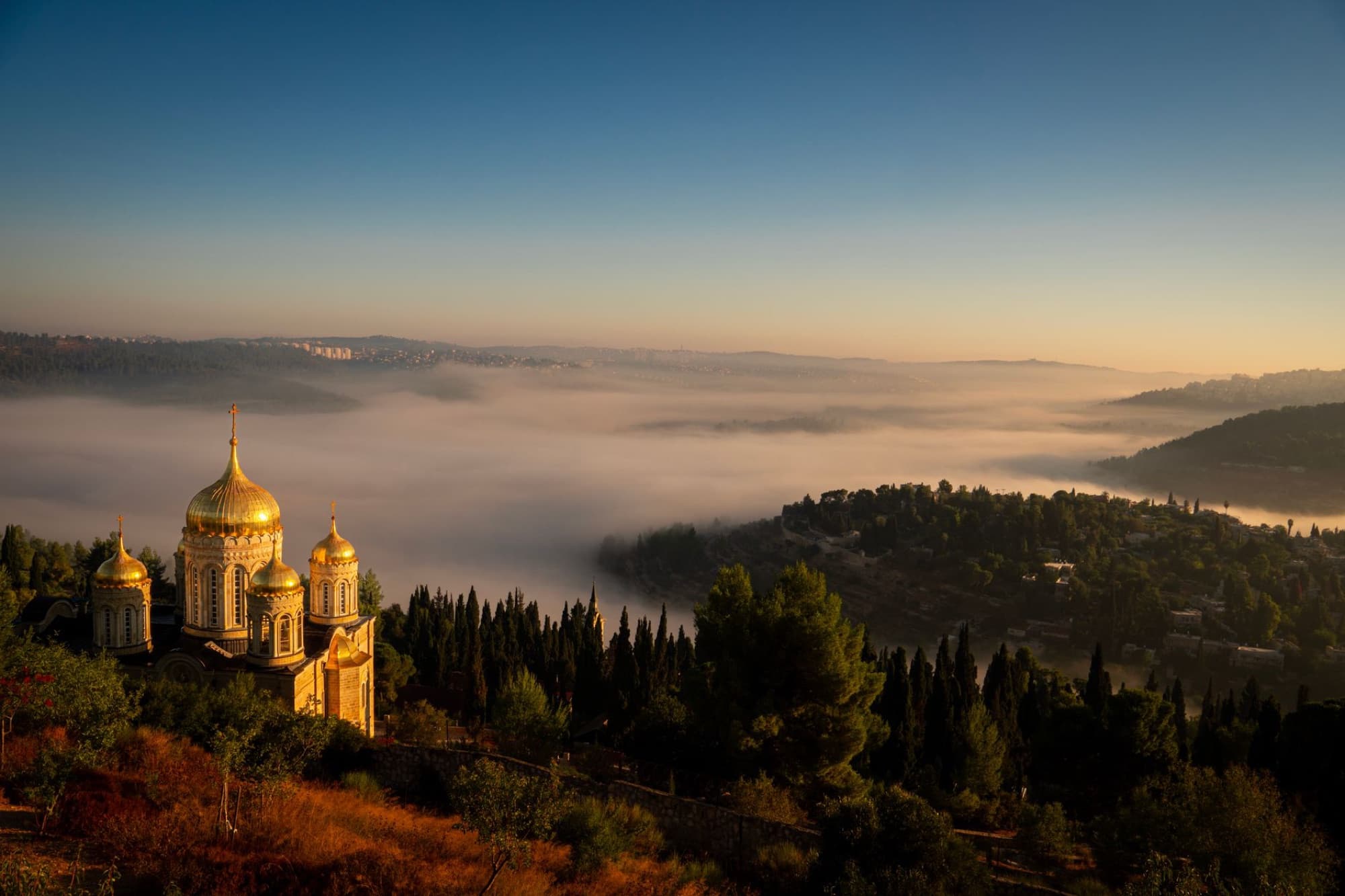 A stunning view of a golden-domed church amidst a foggy landscape during sunrise.