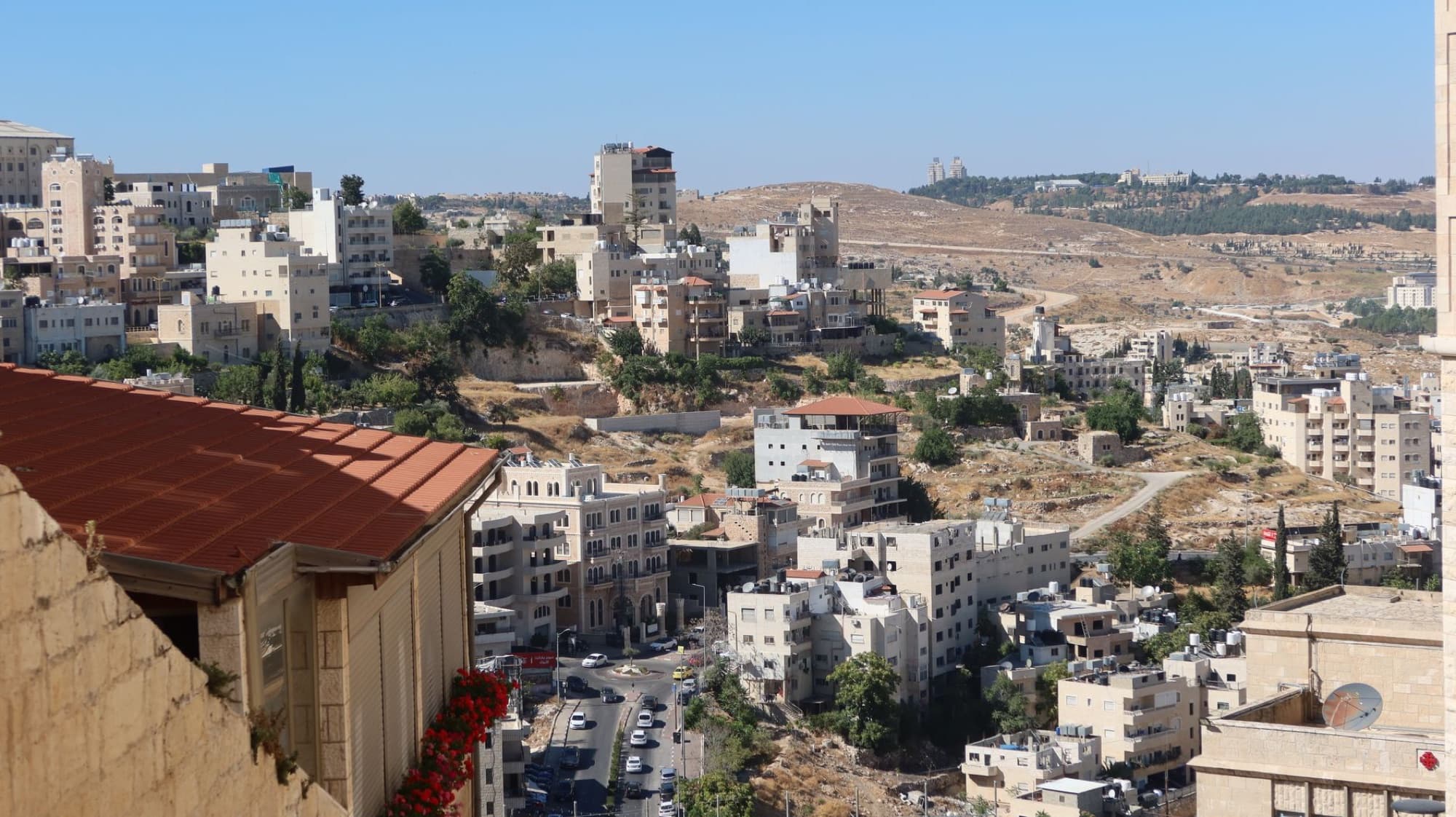 Scenic urban view of Middle Eastern hillside city with diverse architecture and sunny skies.