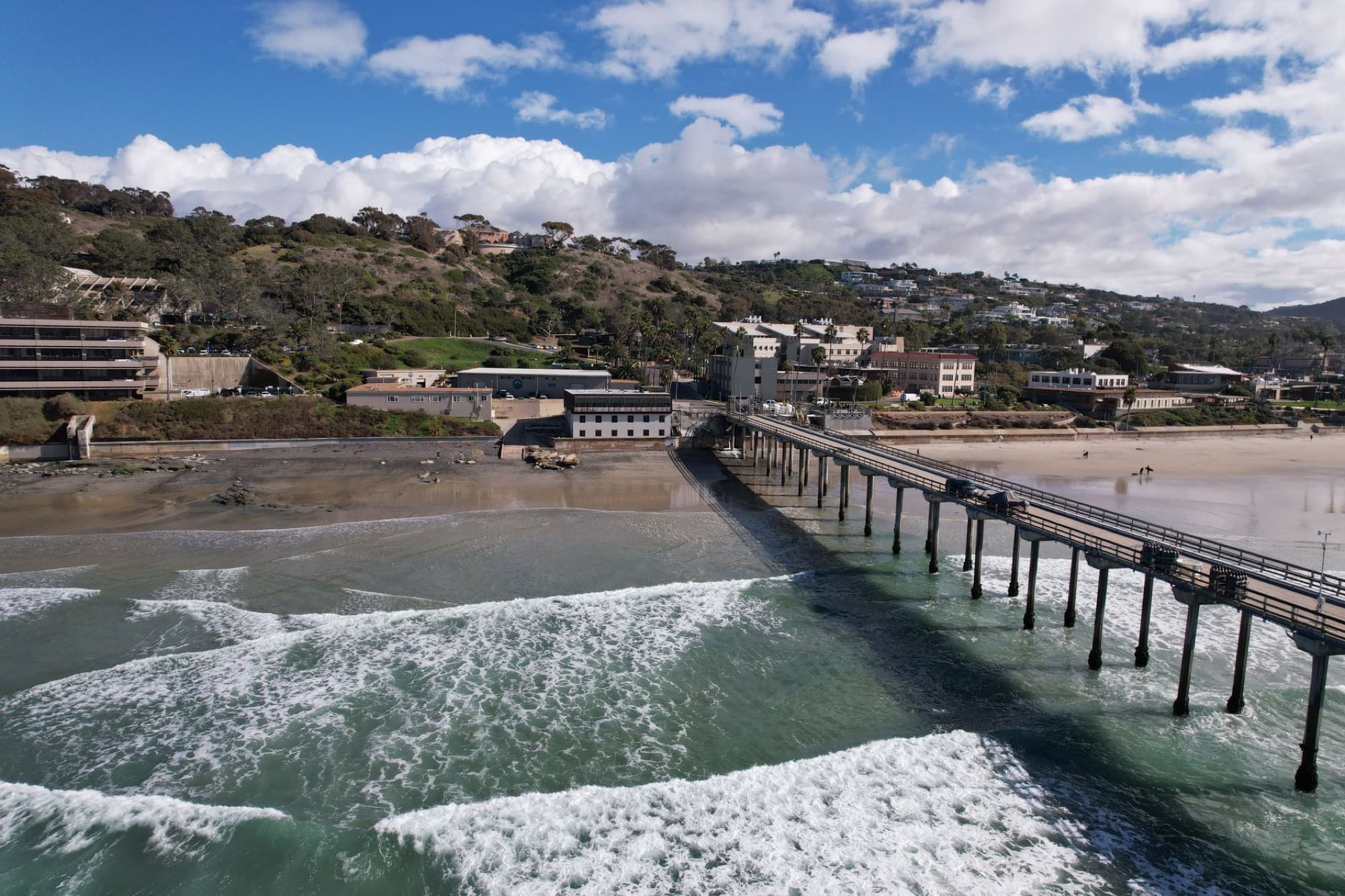 Aerial view of Scripps Pier and La Jolla shoreline with waves crashing on the beach in San Diego, CA.