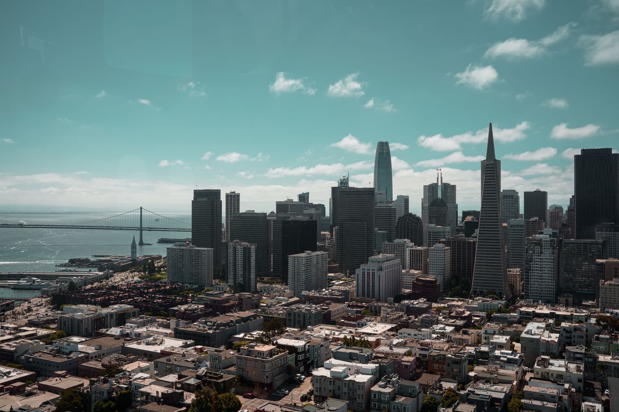 Stunning aerial view of San Francisco's skyline, featuring the iconic Bay Bridge under a bright sky.