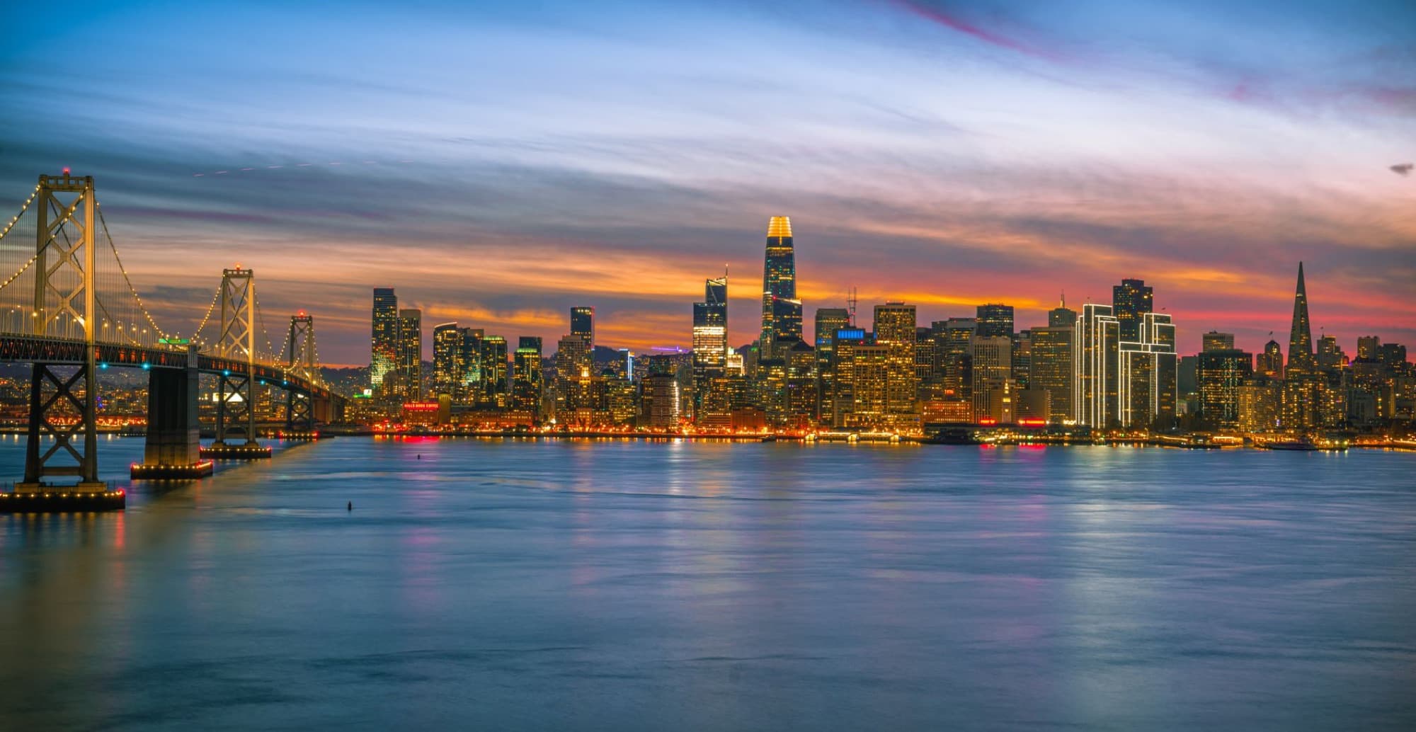 Stunning San Francisco skyline featuring the Bay Bridge during twilight with vibrant city lights reflecting on the water.