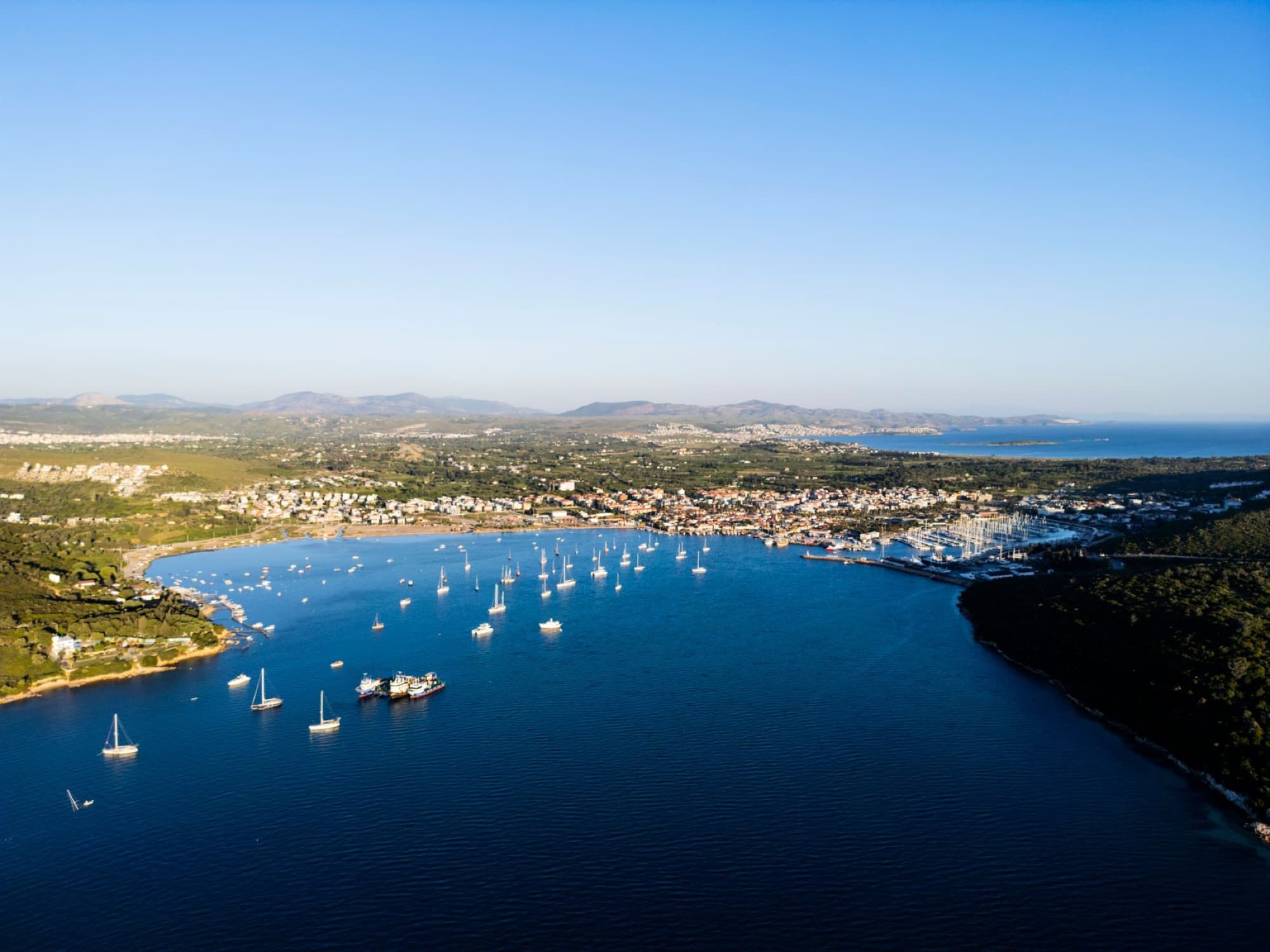 Discover the stunning aerial view of Sığacık Harbor with sailboats under a clear blue sky in İzmir, Türkiye.