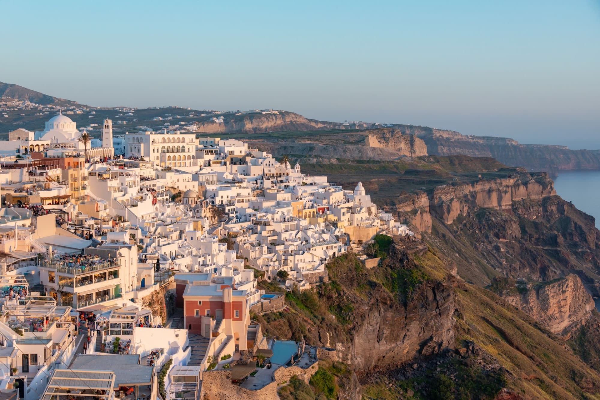 Spectacular aerial view of whitewashed buildings atop the cliffs of Santorini, Greece at sunset.