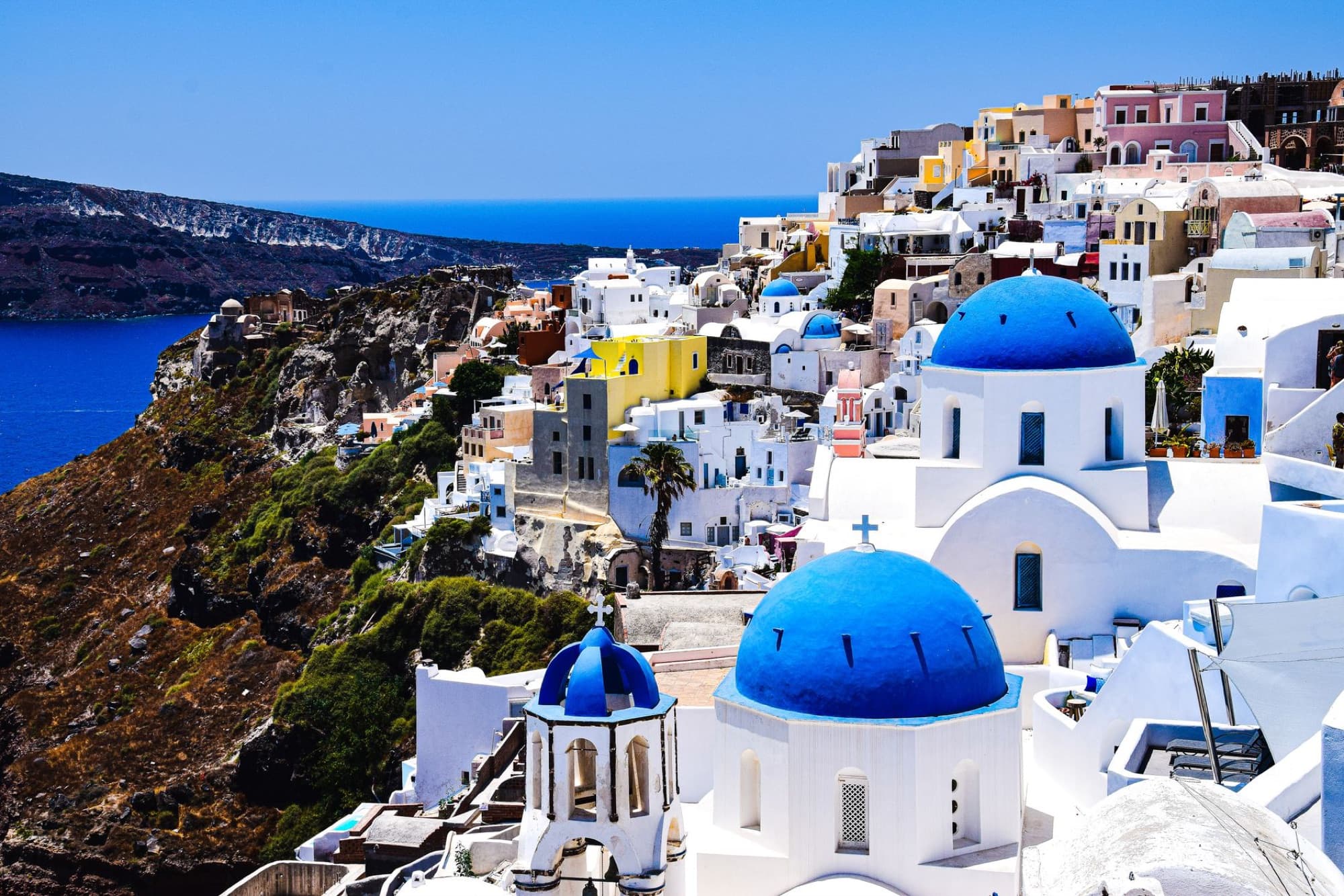 Aerial view of Santorini's famous blue-domed churches and whitewashed buildings overlooking the Aegean Sea.
