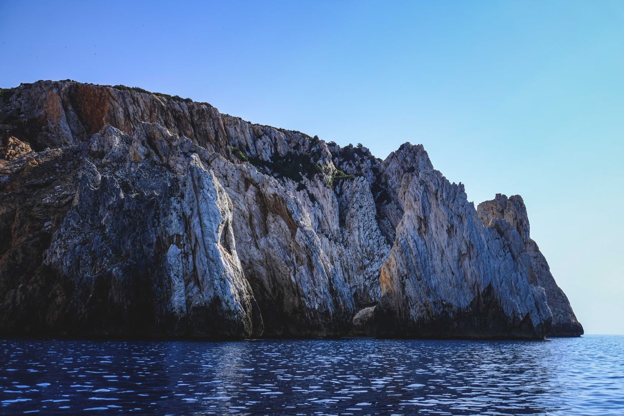 Stunning rock formations at Masua's coastline in Sardegna, Italy, under clear blue skies.
