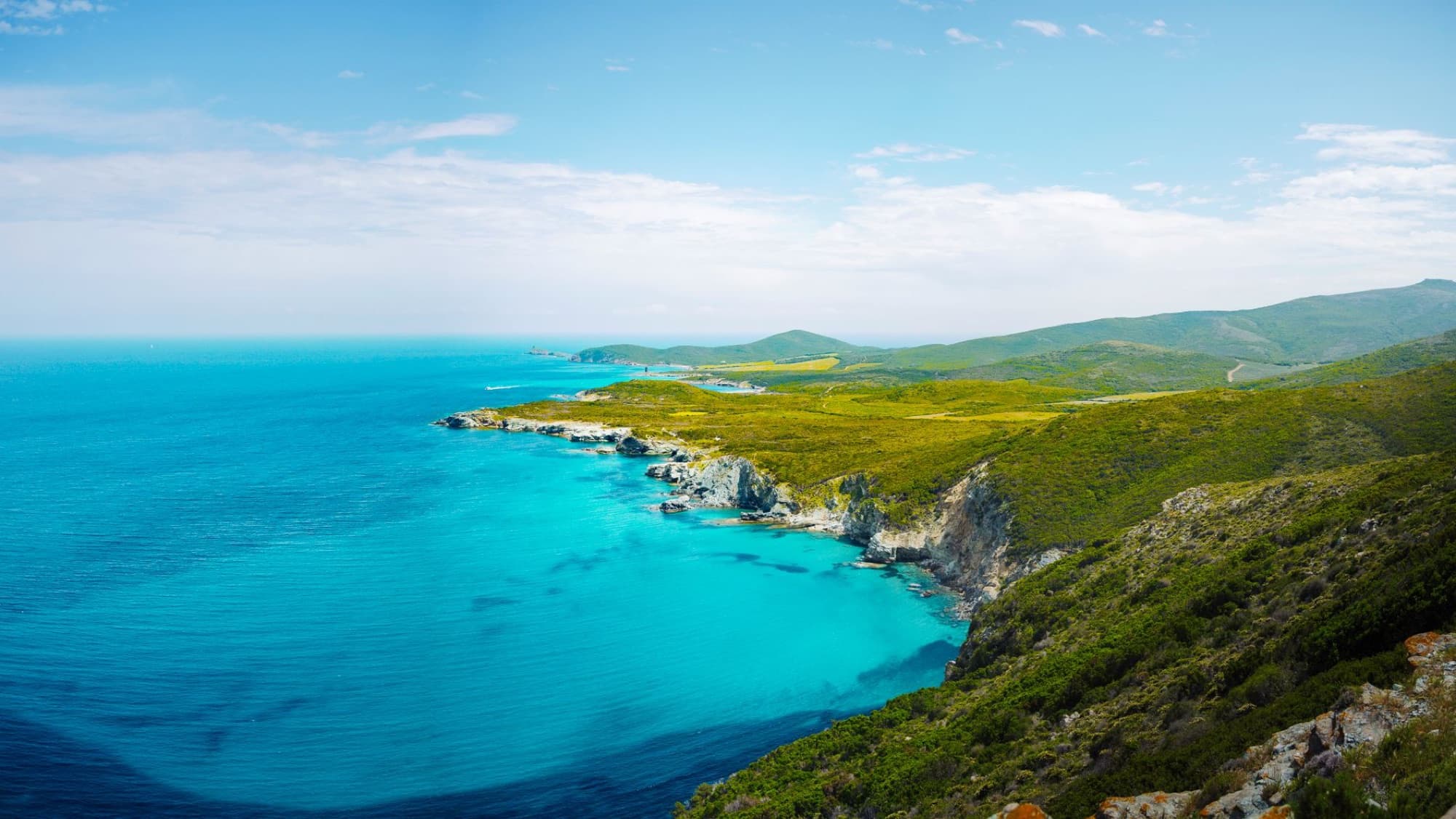 Breathtaking aerial view of the emerald coastline in Cap Corse, France, under a clear blue sky.