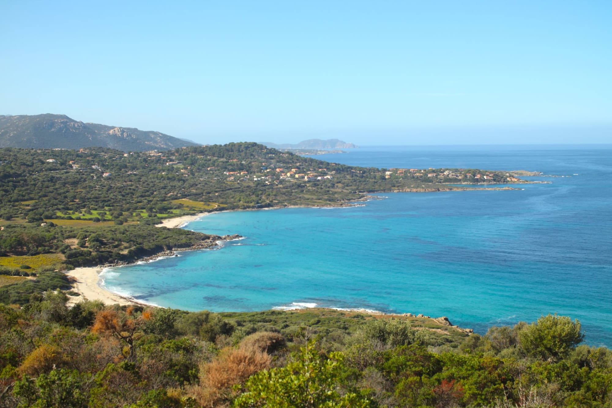 A stunning aerial view of L'Île-Rousse coastline in Corsica, showcasing clear blue waters and lush greenery.