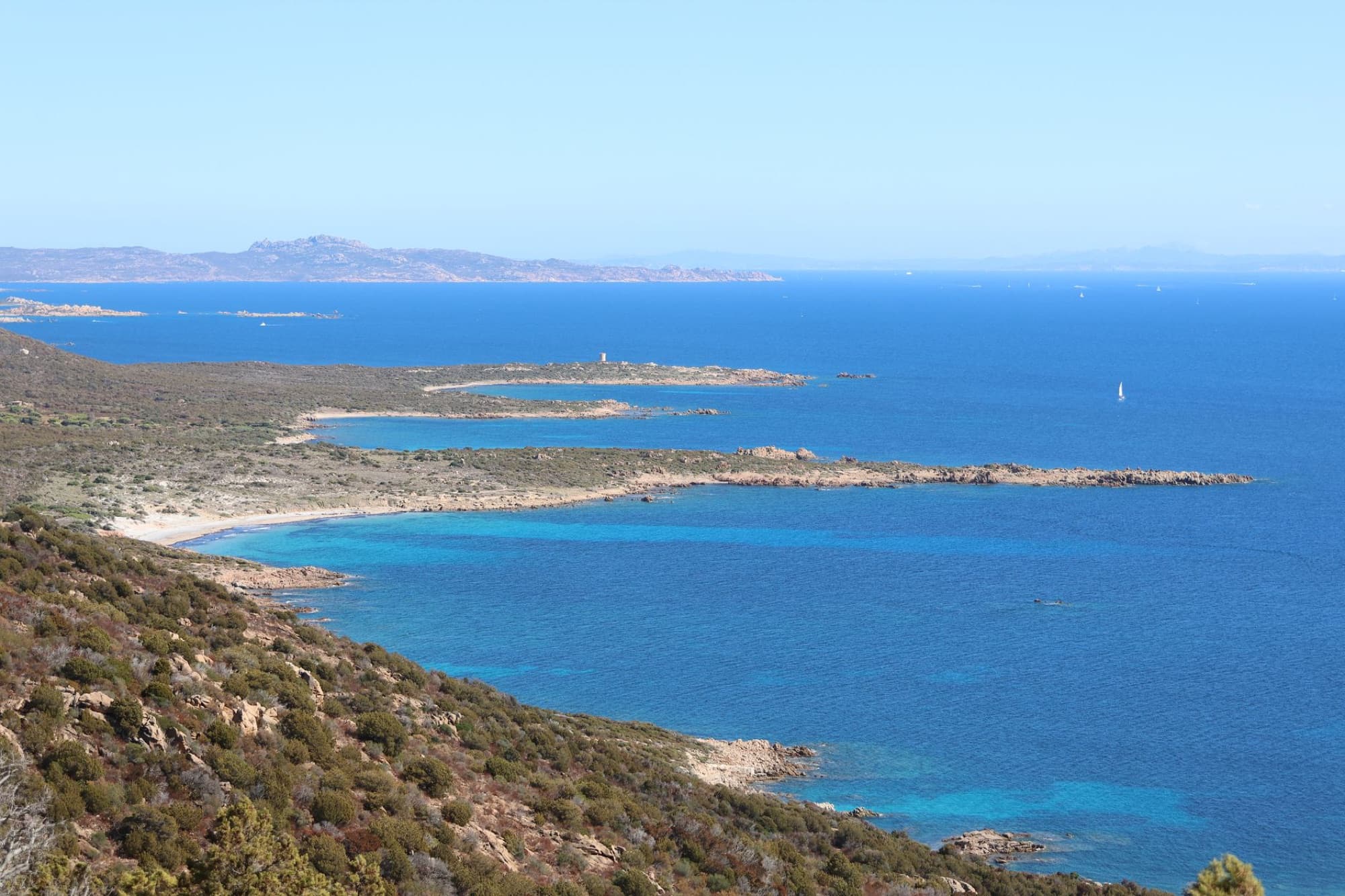 Breathtaking view of Sardinia's coast with clear blue seas, rocky shoreline, and a distant island horizon.