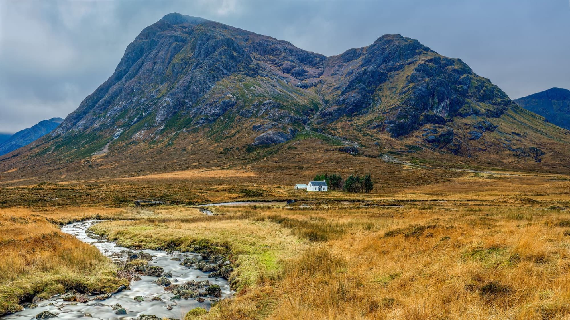 Beautiful landscape view of Scottish Highlands featuring a mountain, river, and countryside house.