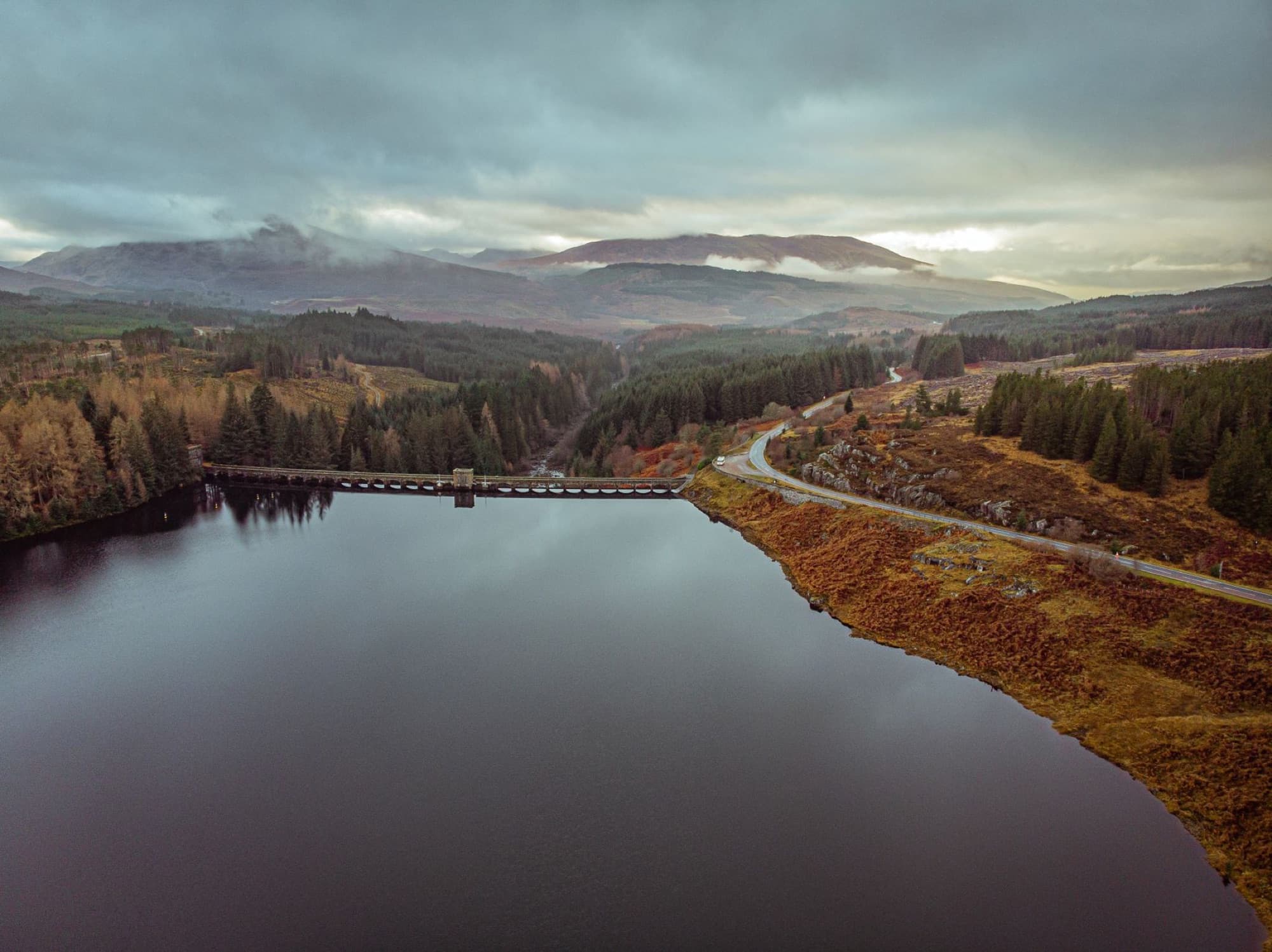 Breathtaking aerial view of a serene lake surrounded by autumn forests in the Scottish Highlands.