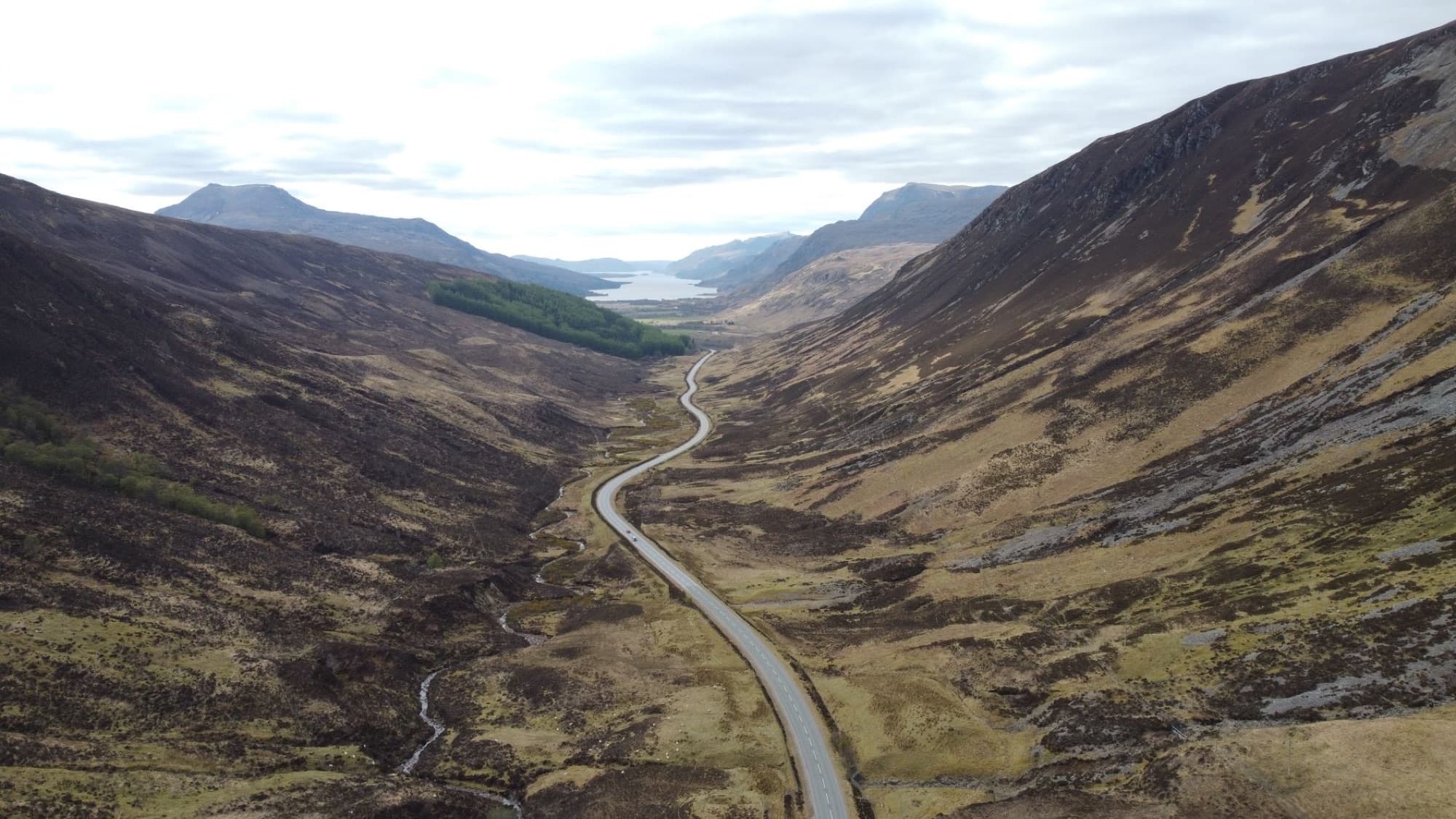 Aerial view of a winding road through a picturesque valley in the Scottish Highlands.