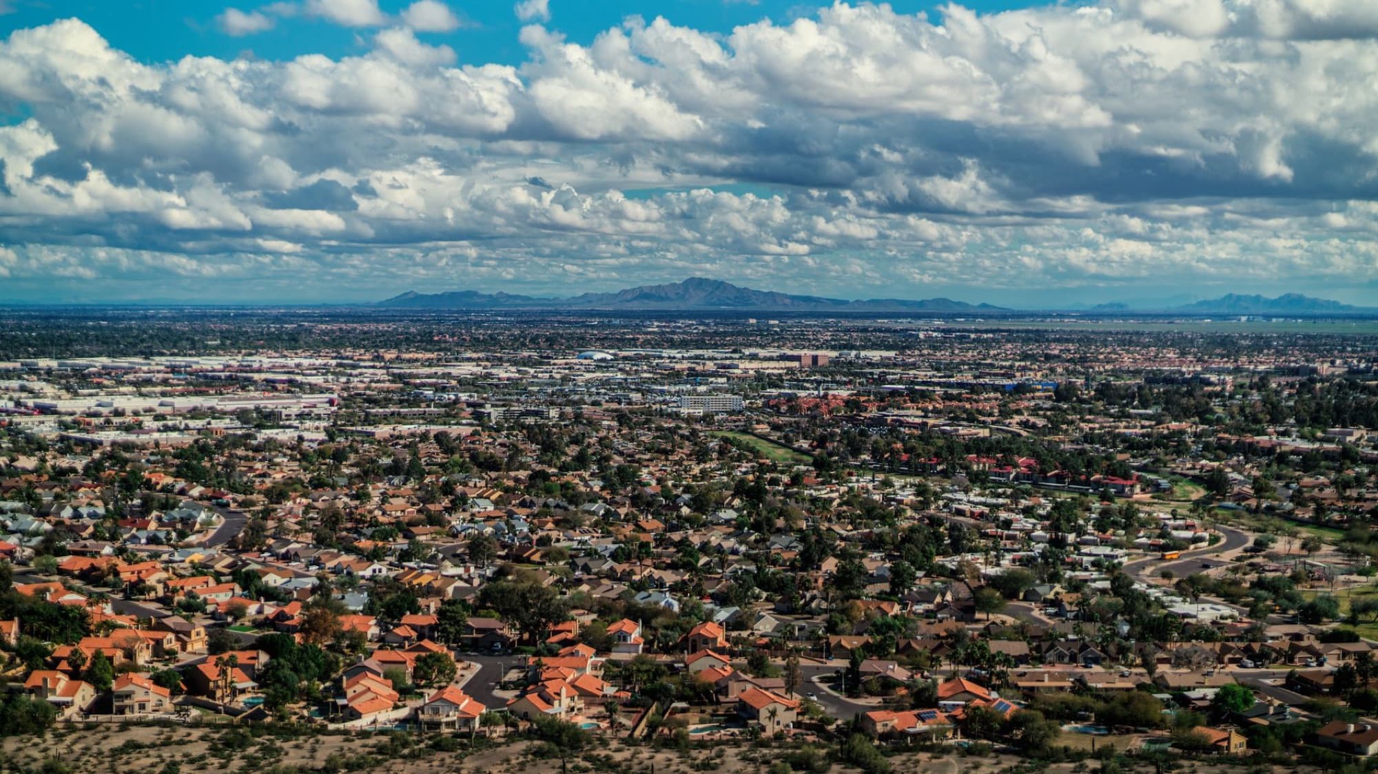 Aerial photo showcasing a city's urban sprawl against a mountain backdrop during daytime.