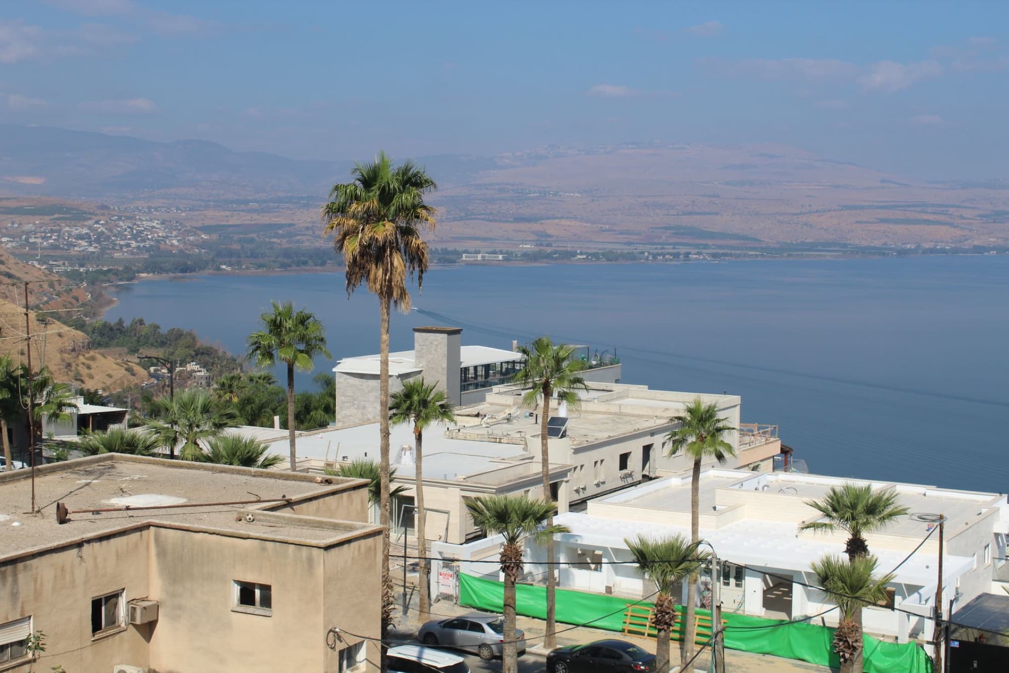 Aerial view of the Tiberias cityscape and the Sea of Galilee, Israel, with palm trees and hills beyond.