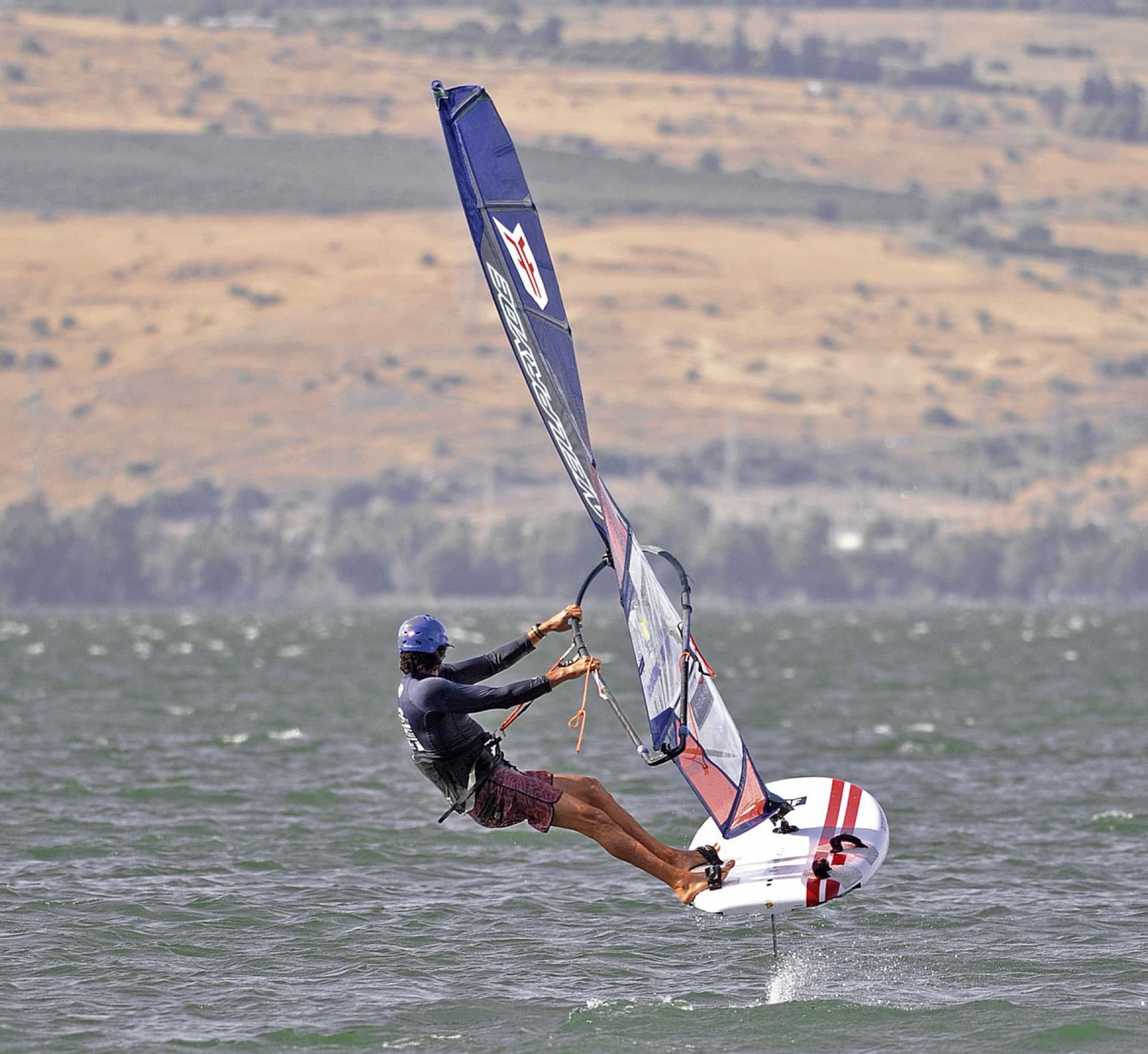 Dynamic windsurfing action on the Sea of Galilee in Tiberias, showcasing skill against a scenic backdrop.
