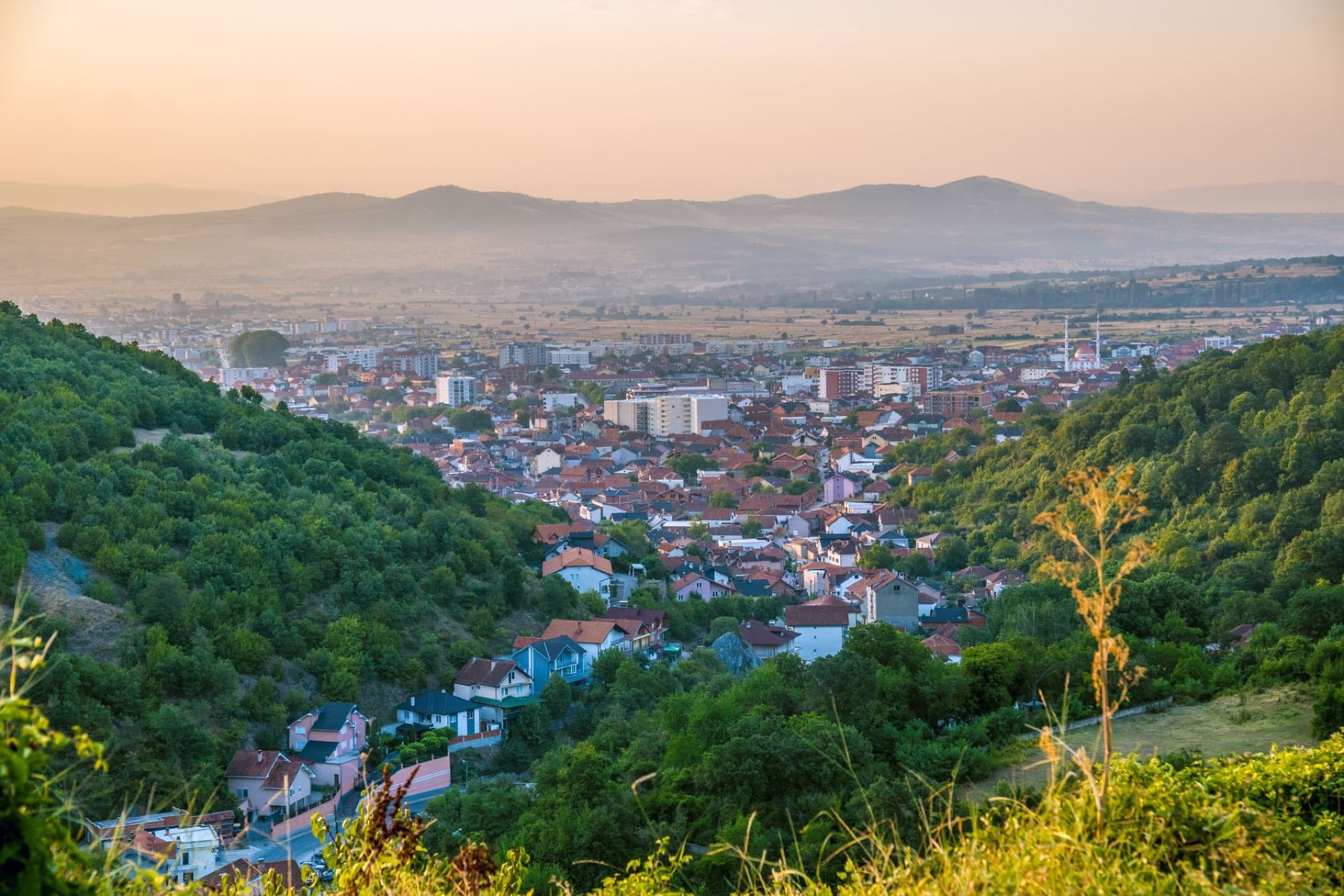 Scenic view of the town of Preševo surrounded by lush hills in Serbia at sunset.